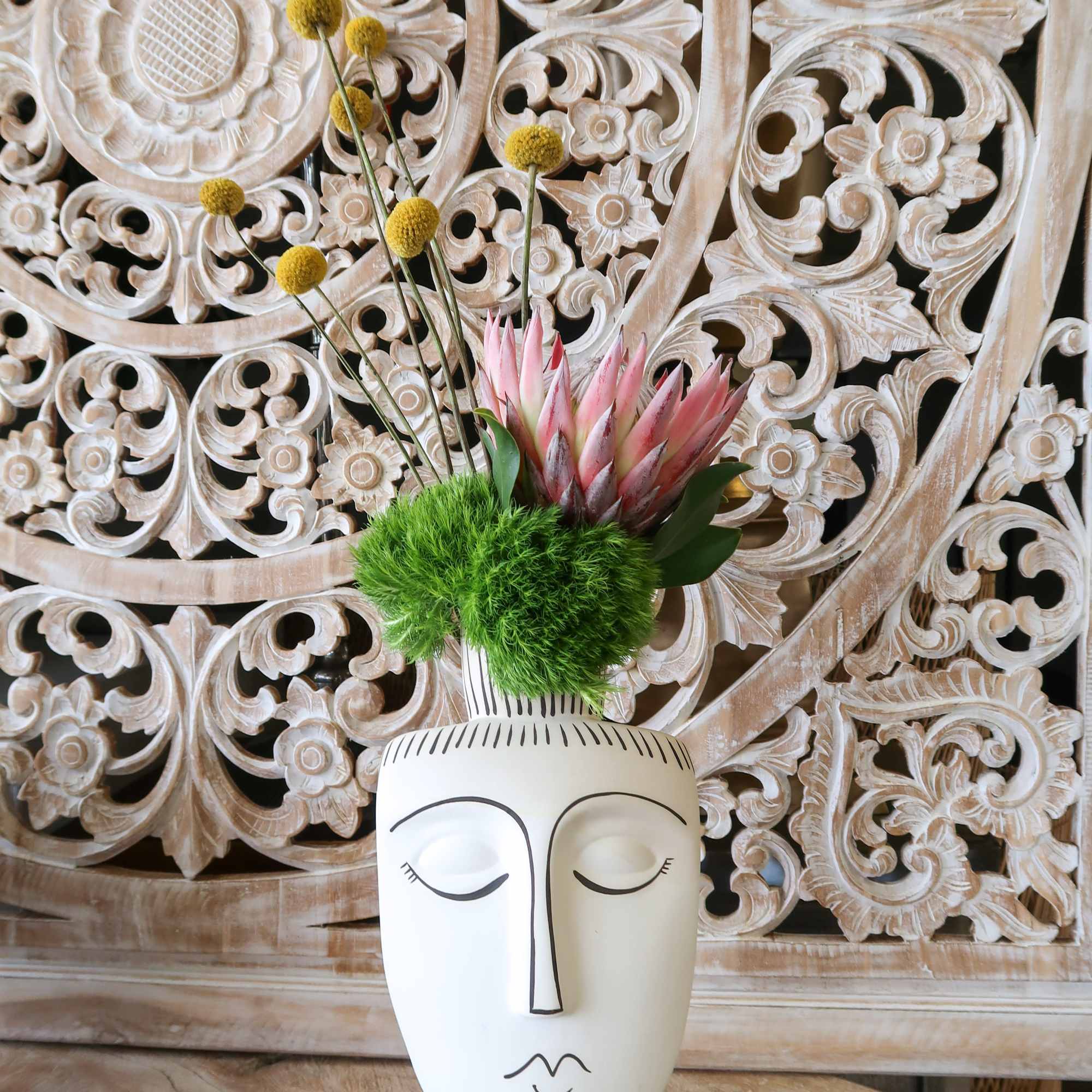 Pink protea arrangement in a white face vase with yellow pom-pom stems