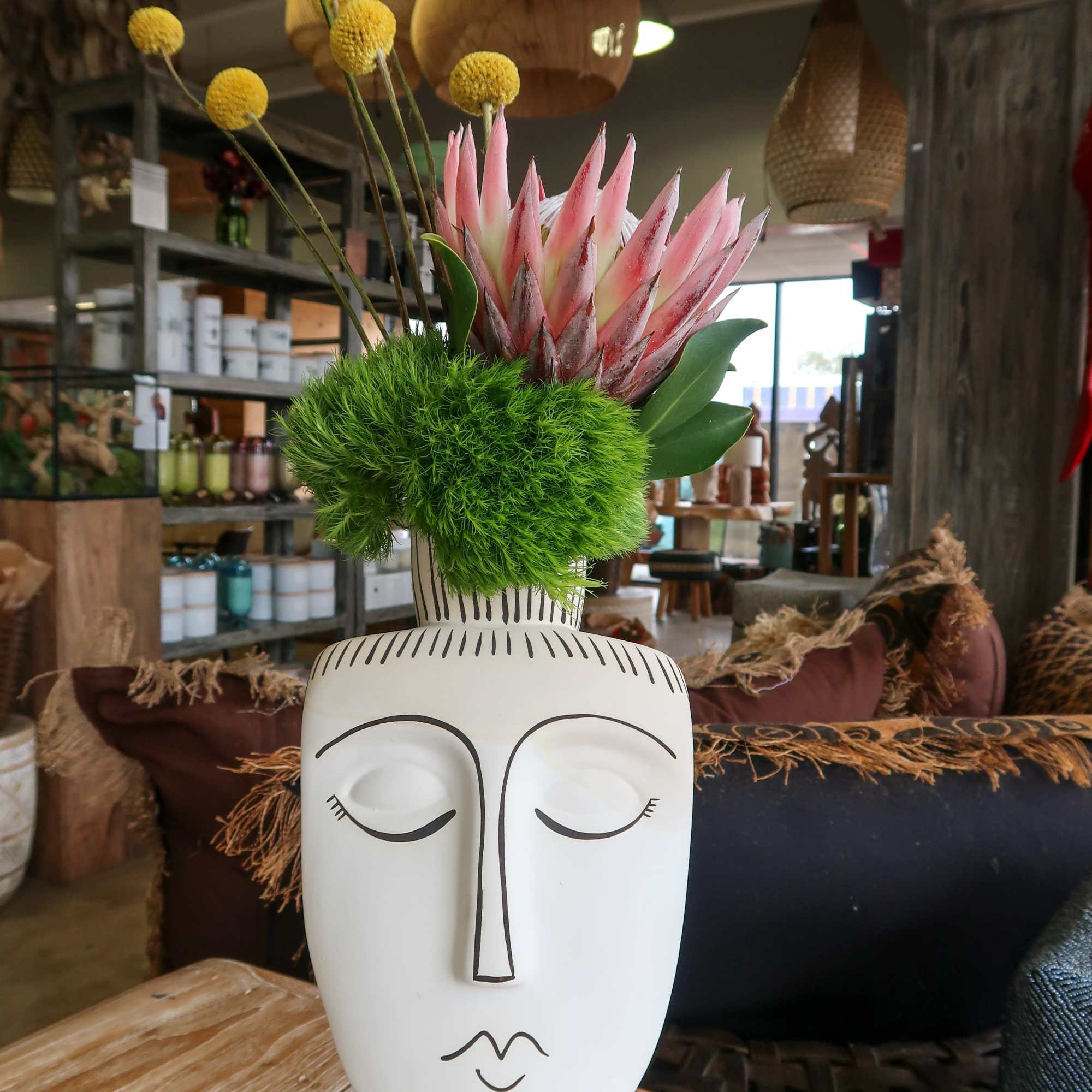Pink protea and yellow pom-pom flowers in a white face vase.