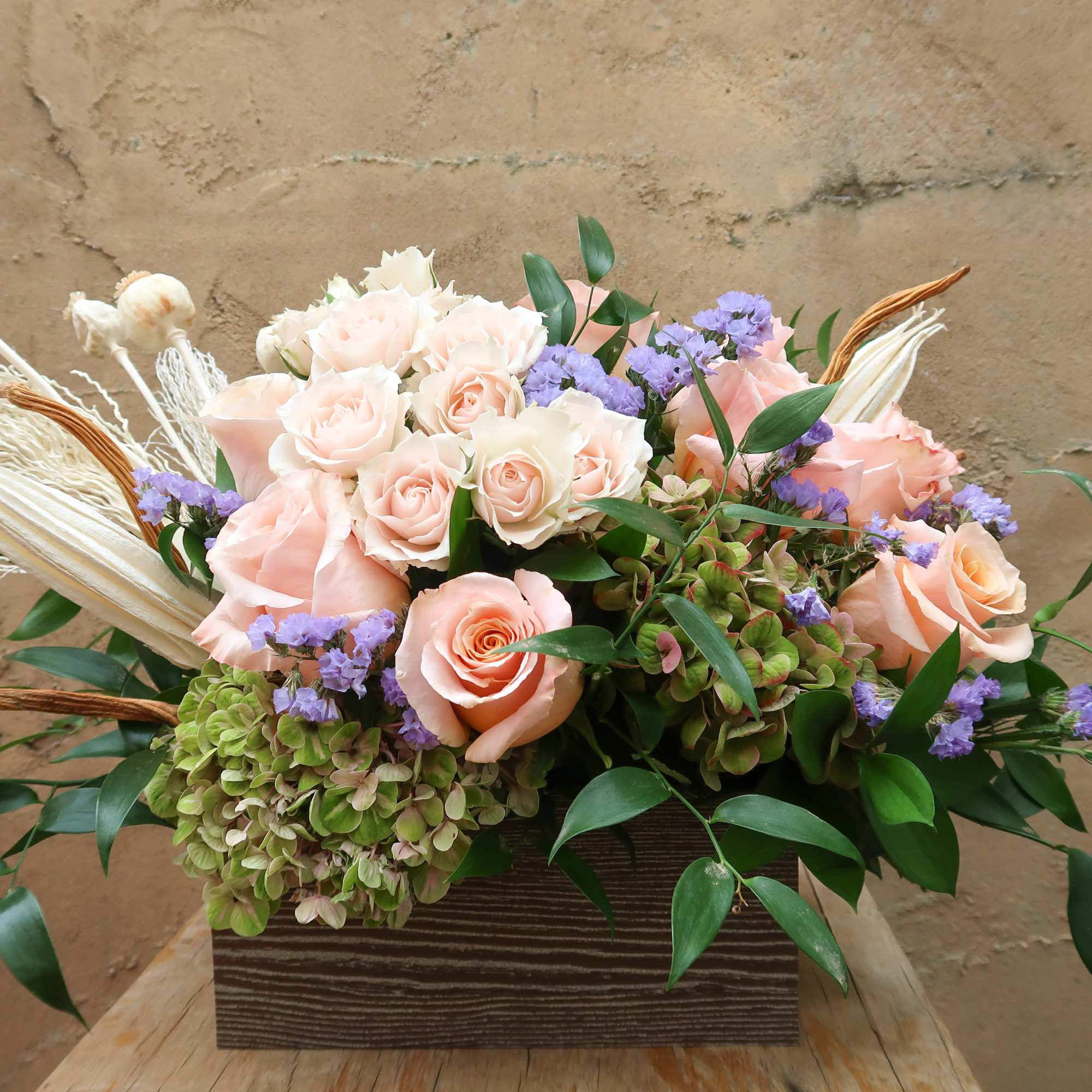 Peach and white roses in a wooden box with purple accents