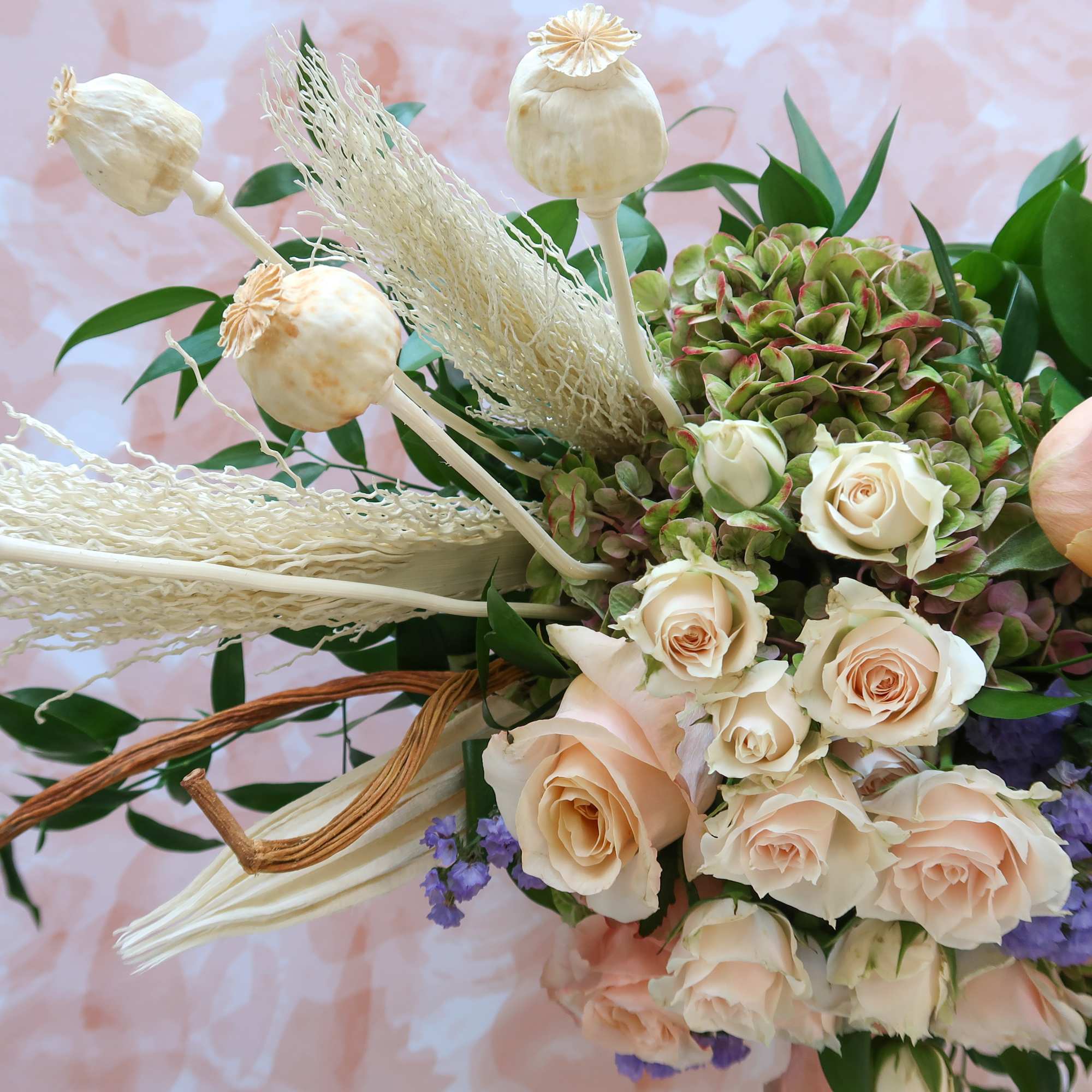 Bouquet of pale peach roses with cream poppy pods and purple filler flowers