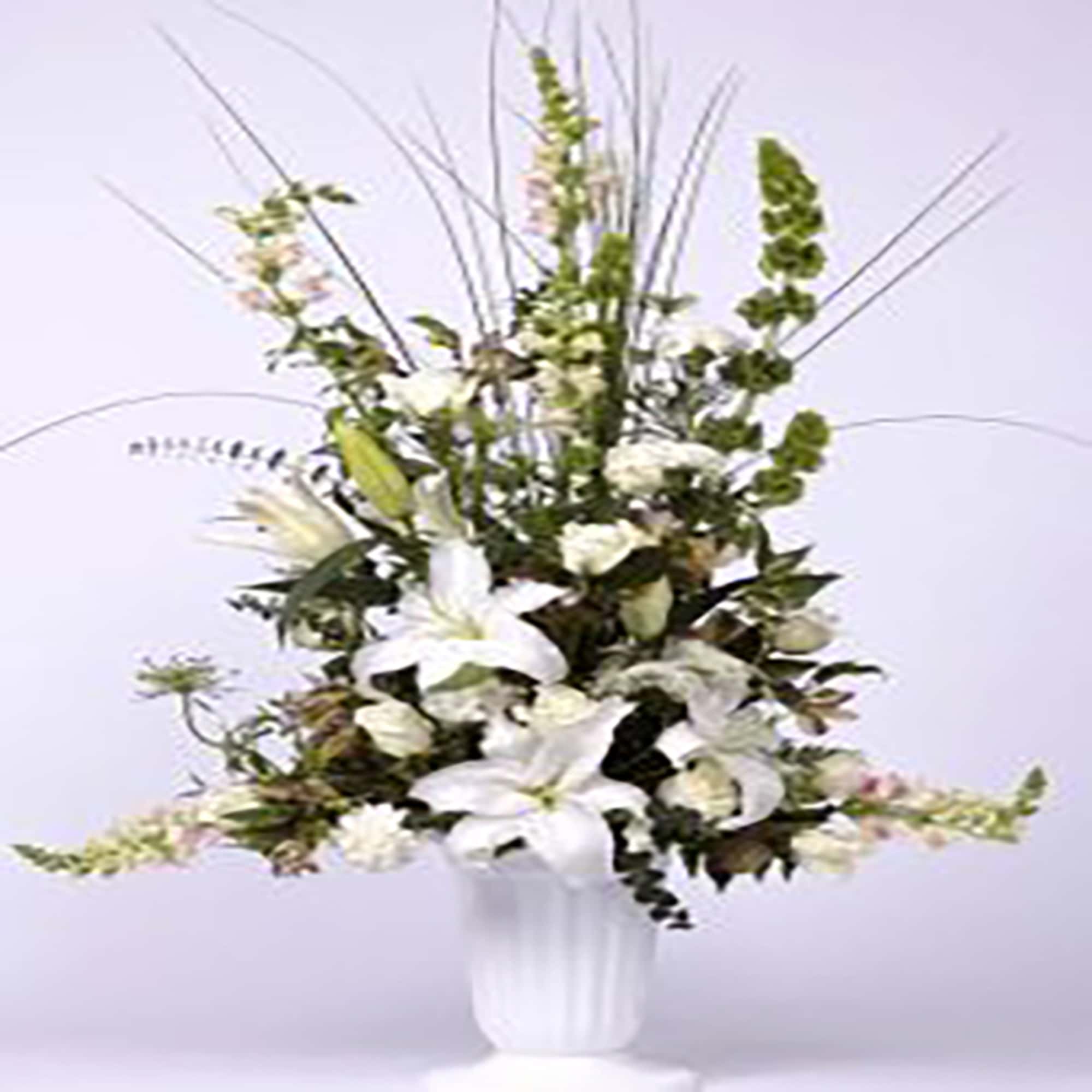 Tall white arrangement of lilies, carnations, and snapdragons in a white pedestal vase