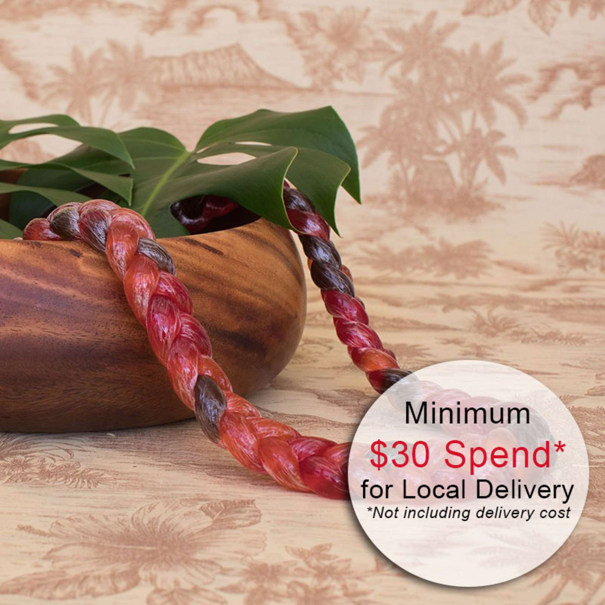 Braided red and orange candy lei draped over a wooden bowl with large tropical leaves.