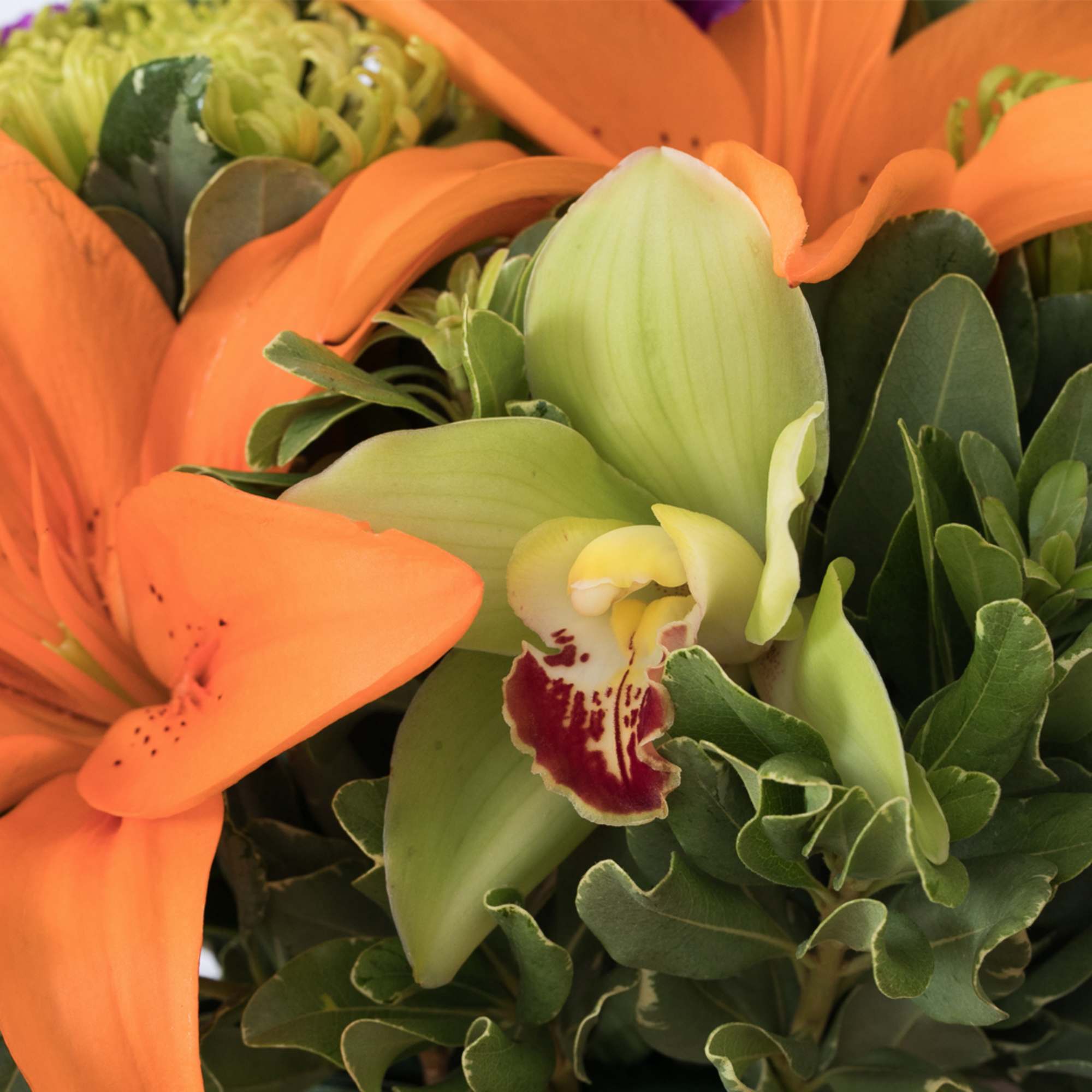 Close-up of orange lilies and green cymbidium orchid in a mixed floral arrangement