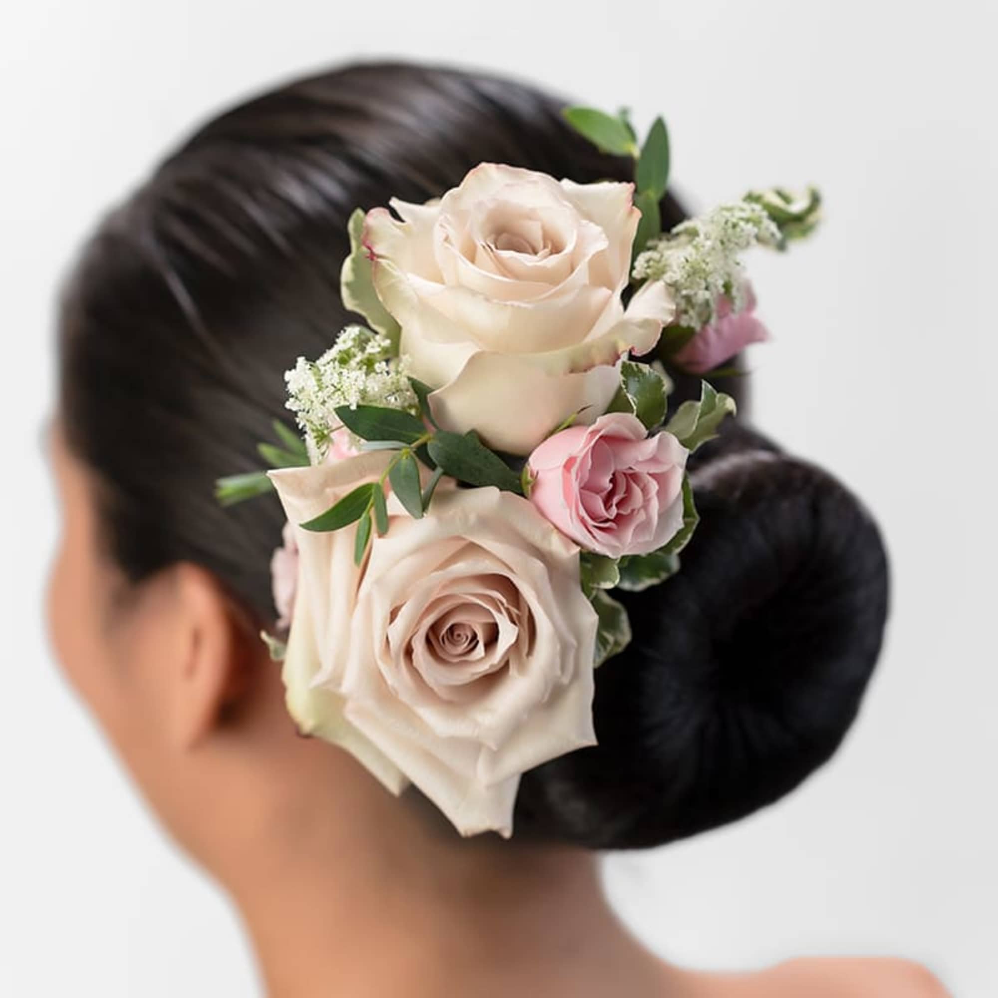 Blush and pink roses arranged as a floral hairpiece on a sleek dark bun.