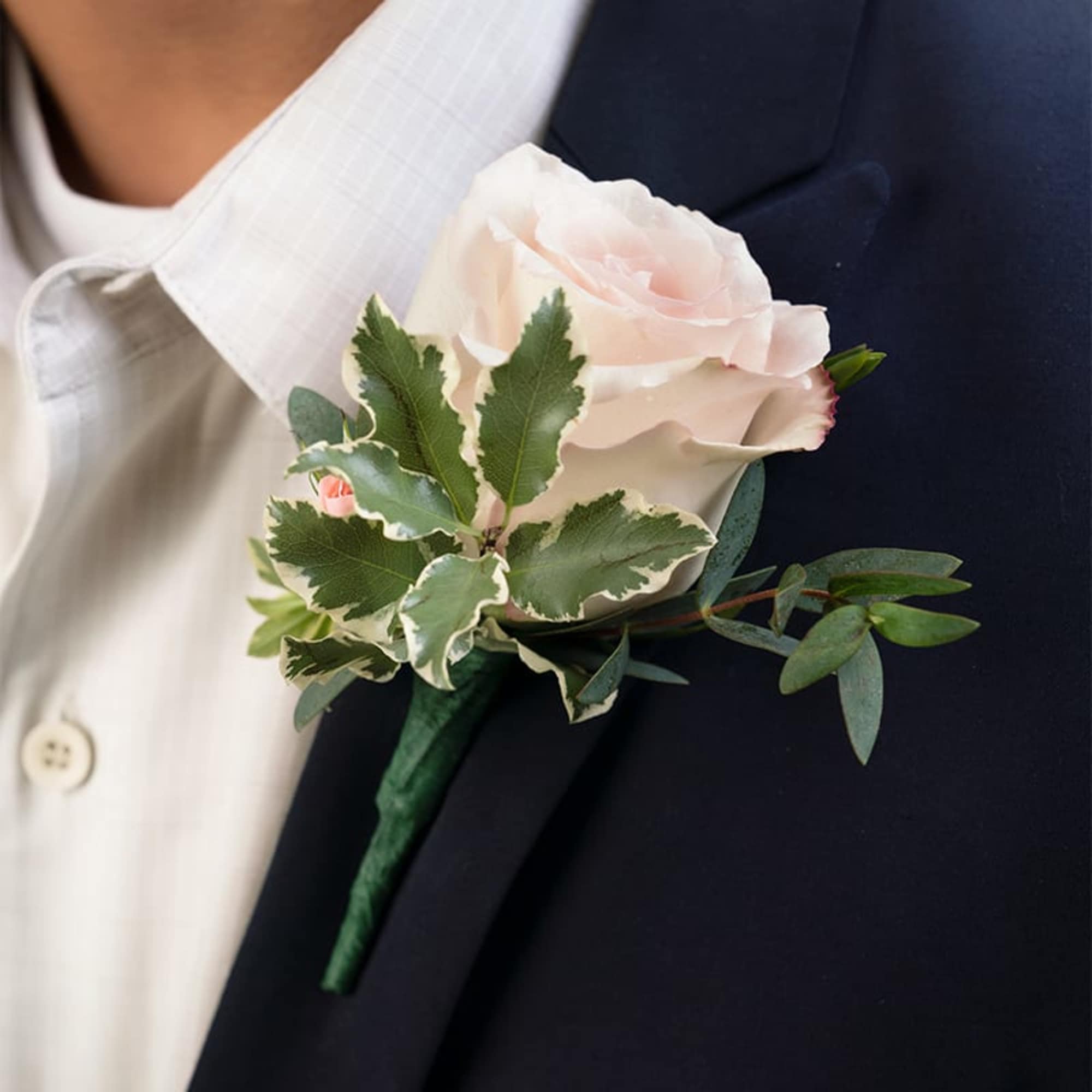Single pale pink rose boutonniere pinned to a dark suit lapel