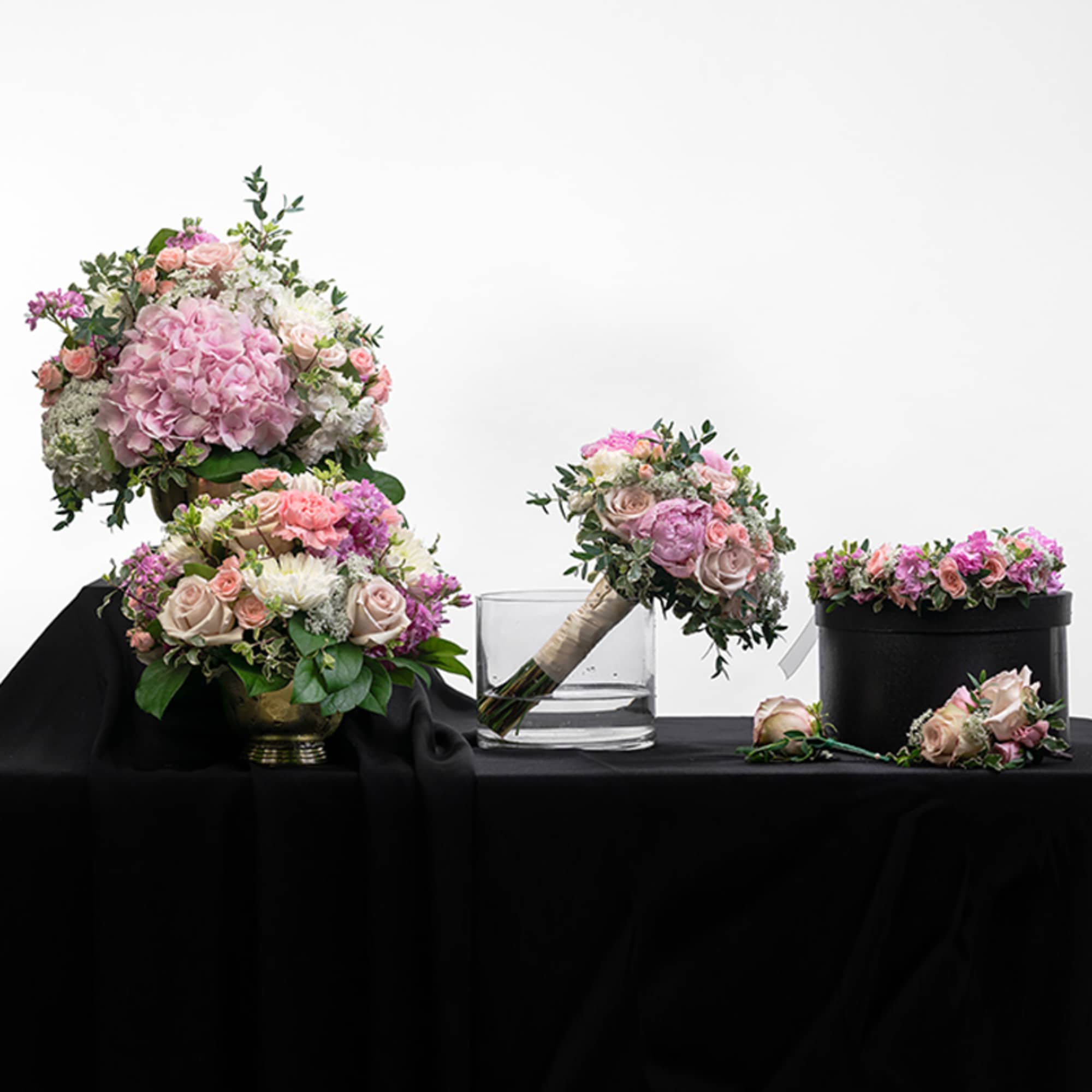 Set of pink and white rose and hydrangea wedding arrangements and bouquets displayed on a black cloth.