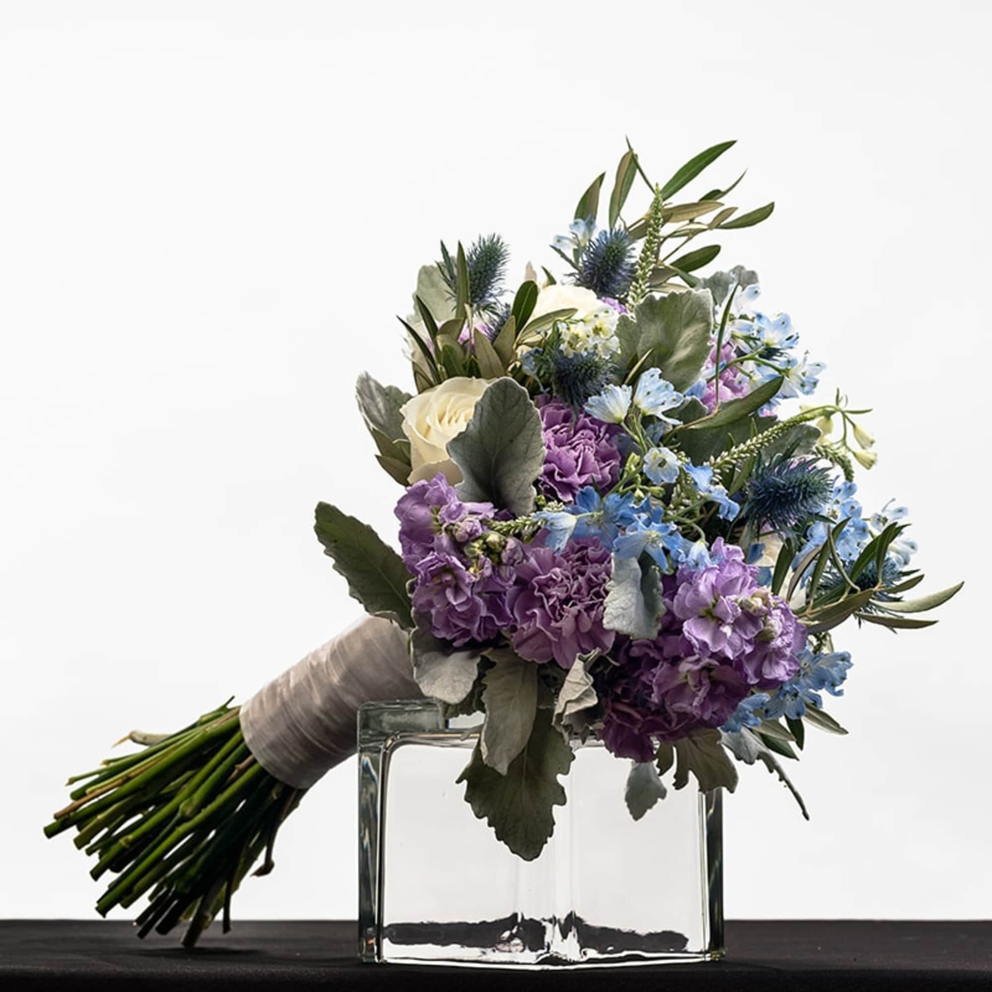 Hand-tied bouquet of purple, blue, and white flowers resting on a clear glass vase.