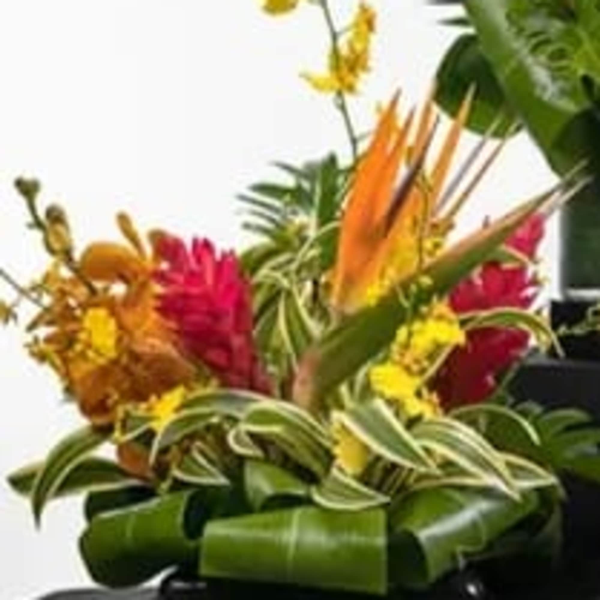 Tropical arrangement of orange and yellow flowers with folded green leaves in a low black bowl