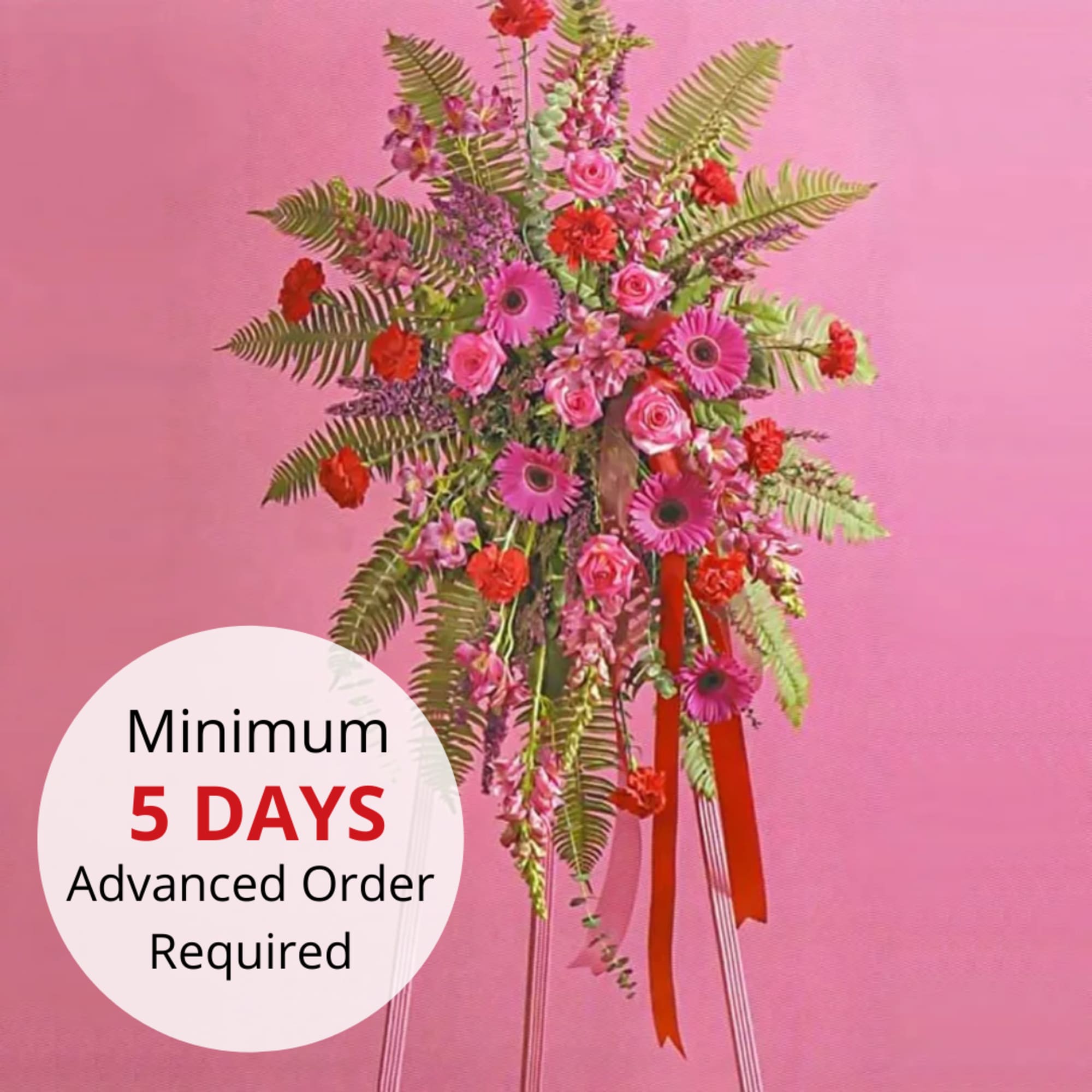 Tall standing spray of pink and red flowers with ferns on a tripod stand