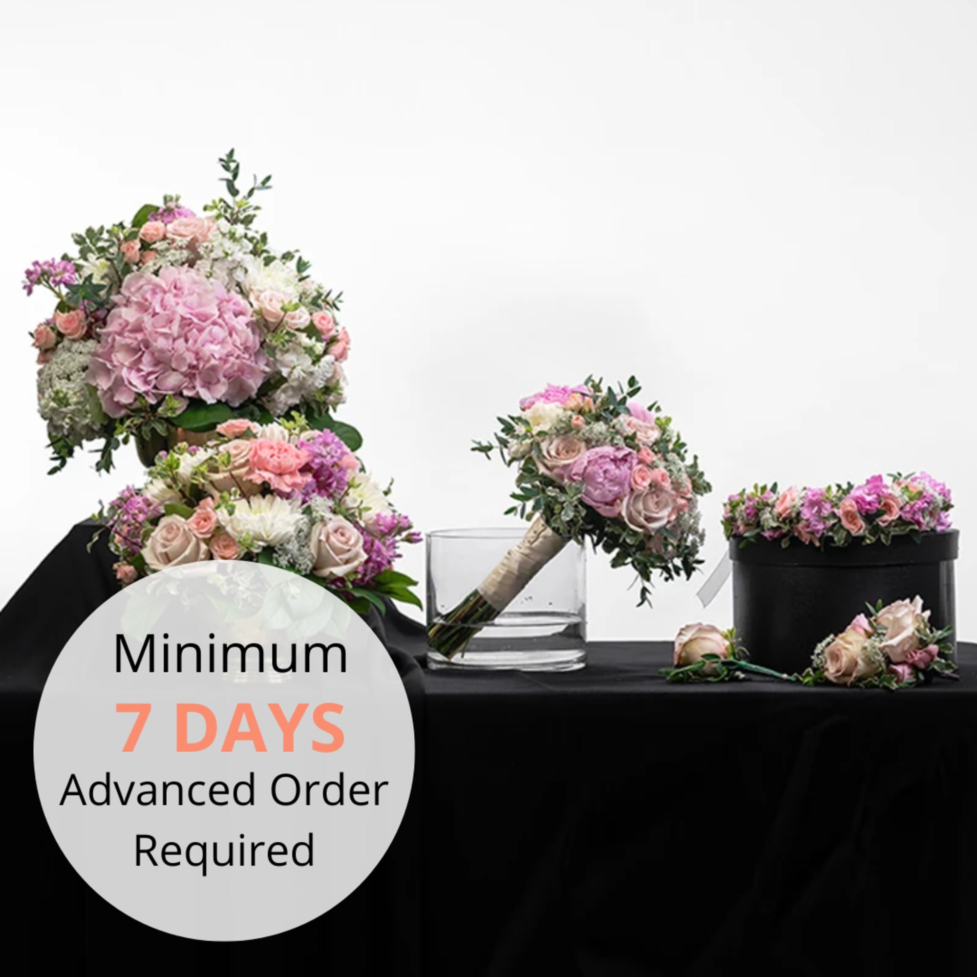 Set of pastel pink and white rose and hydrangea wedding bouquets and floral crown on black cloth.