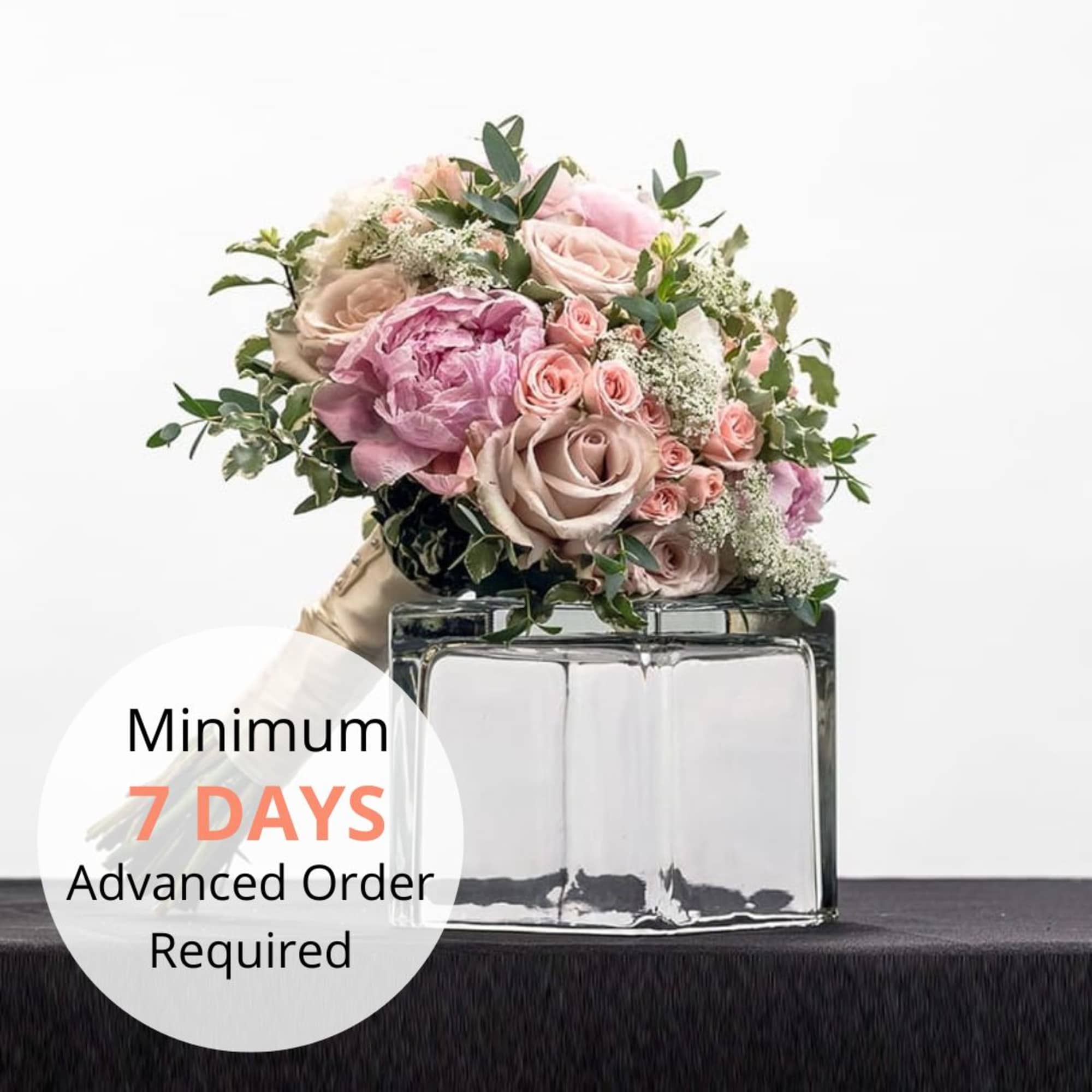 Hand-tied bouquet of blush and pink roses and peonies resting on a clear glass cube vase.
