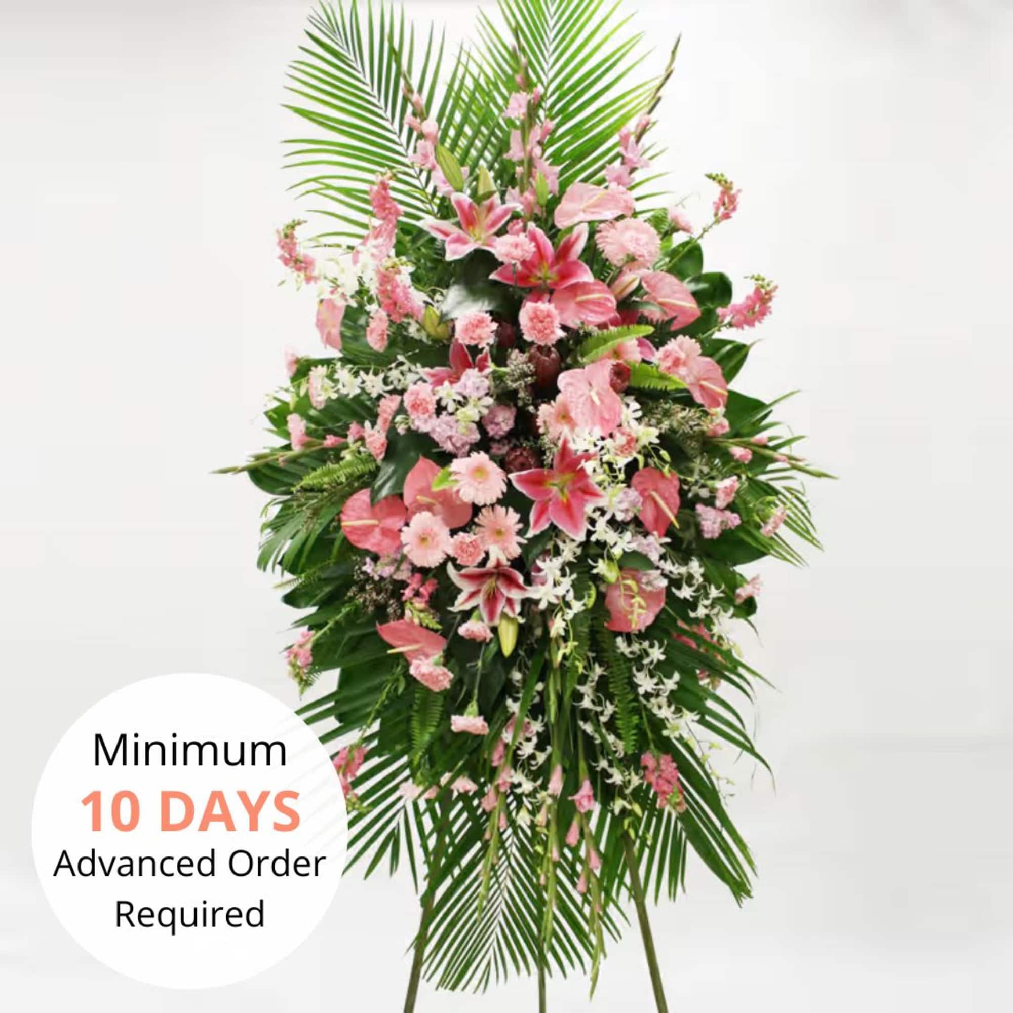 Tall standing spray of pink lilies and mixed flowers on a green palm leaf backdrop.