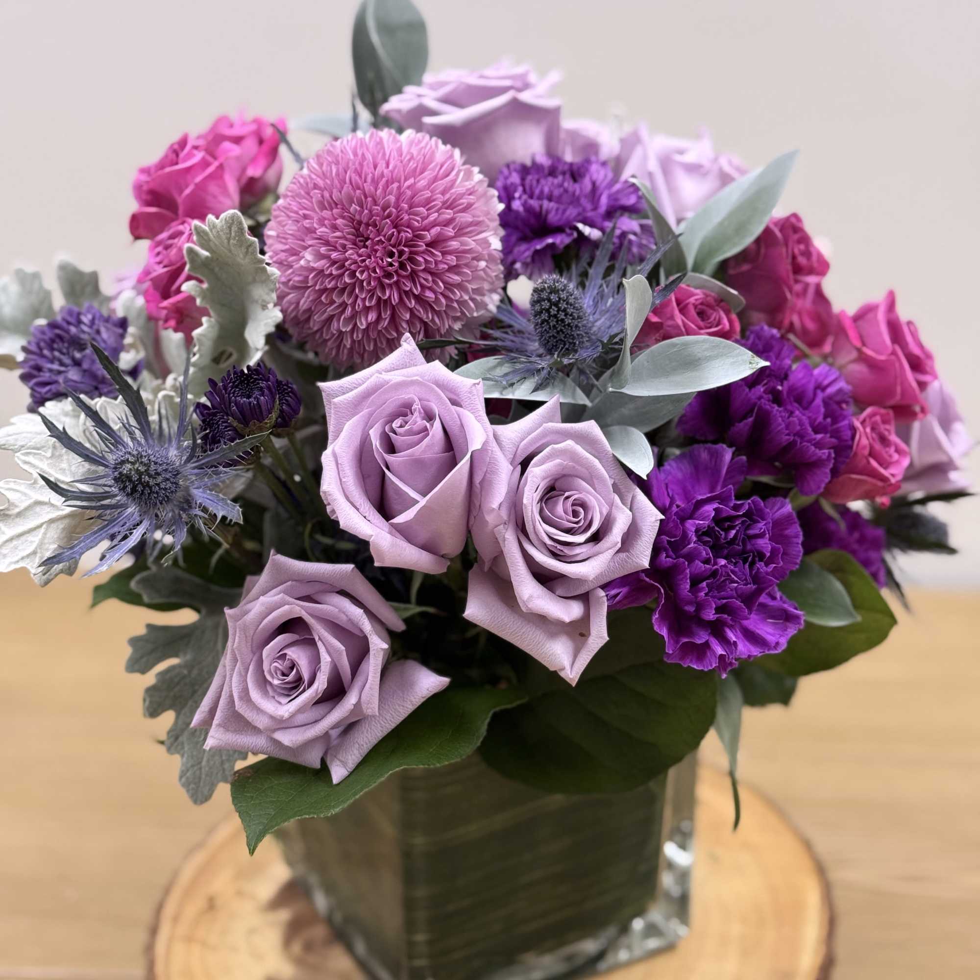 Lavender and purple flower arrangement with roses and carnations in a glass cube vase.