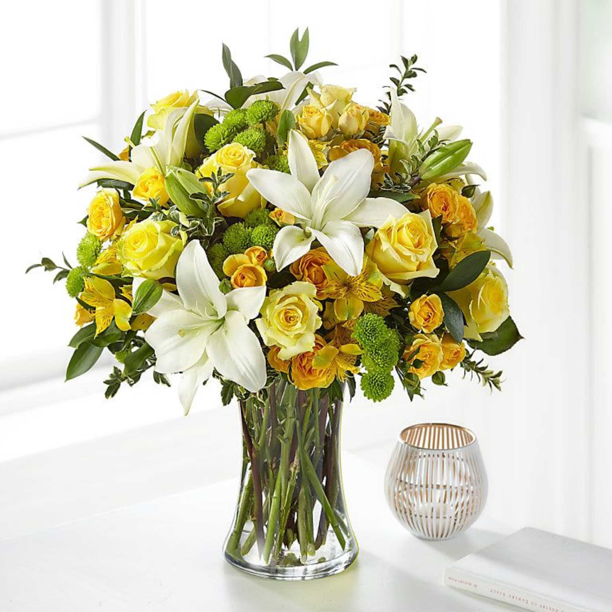 Yellow roses and white lilies arranged in a clear glass vase