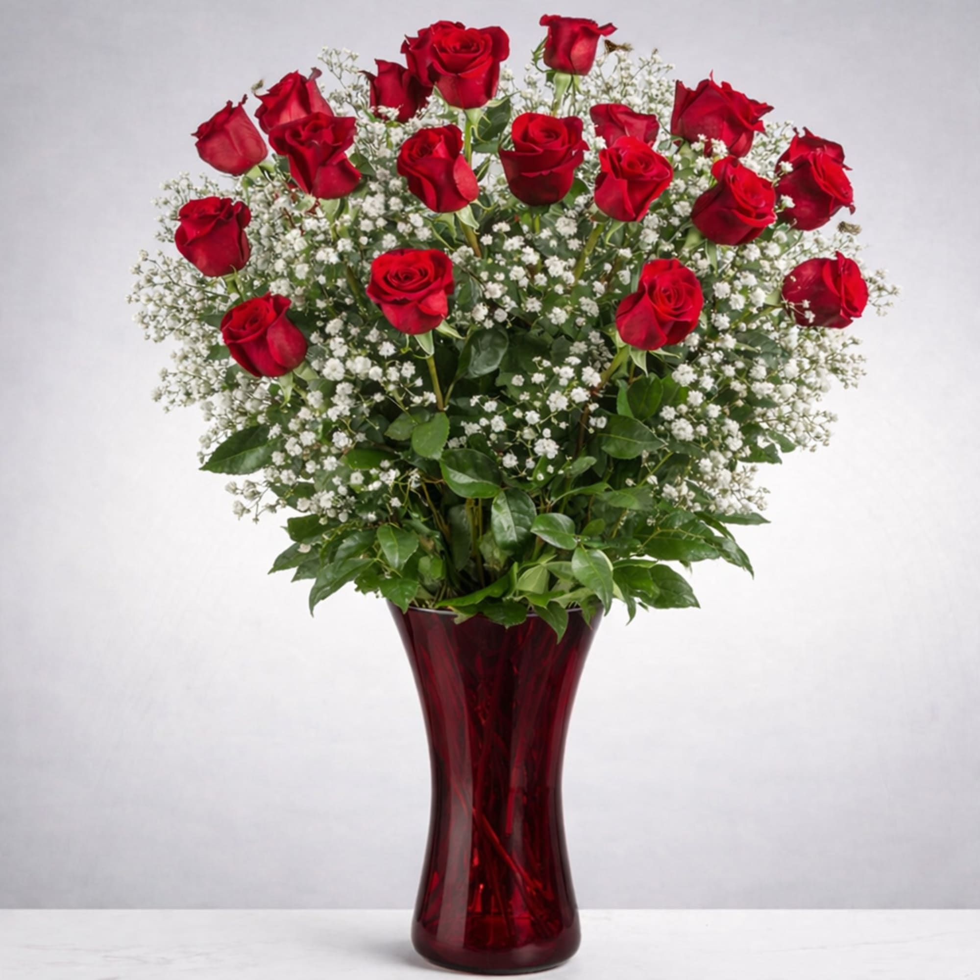 Red roses arranged in a tall red glass vase with white filler flowers