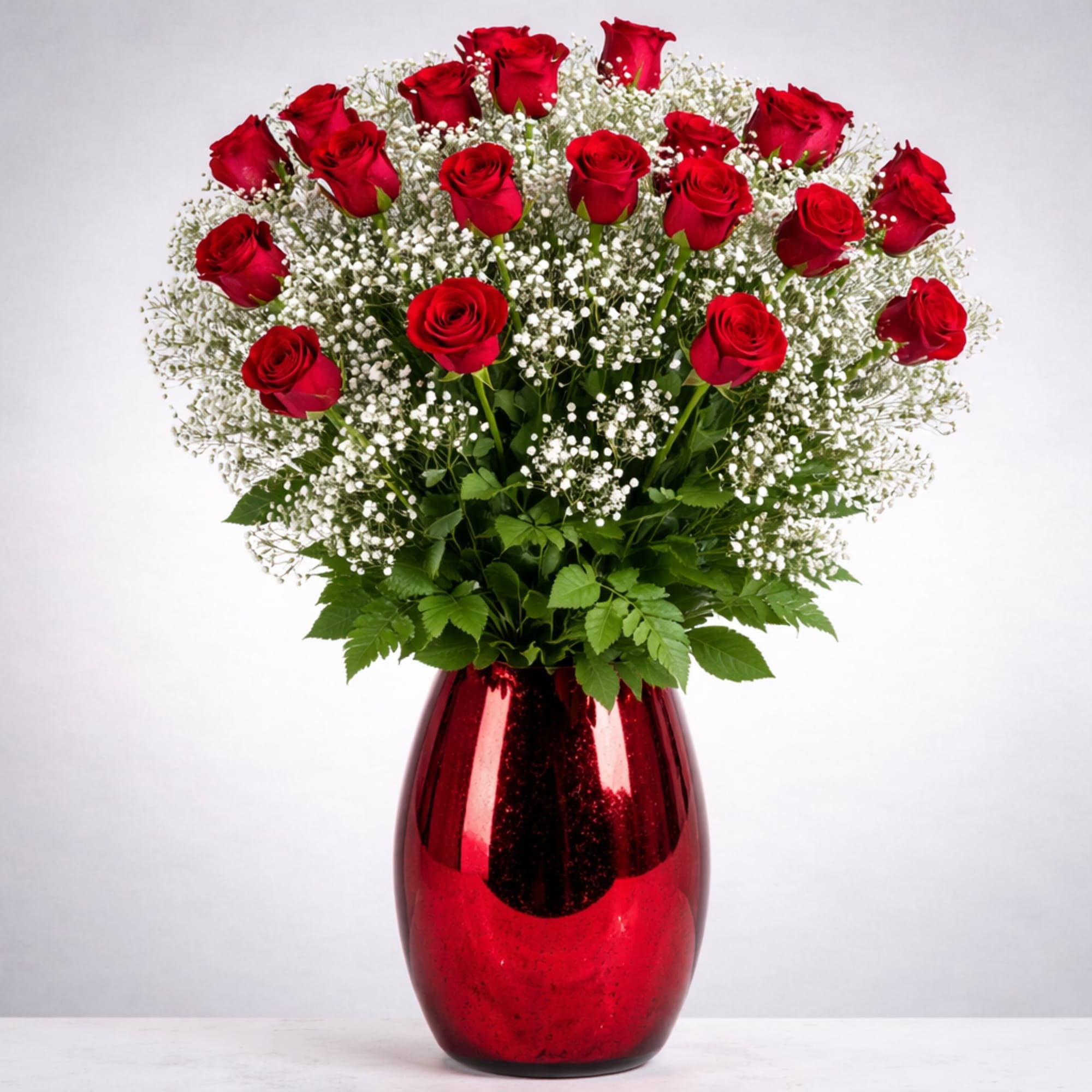 Red roses arranged in a red vase with white filler flowers