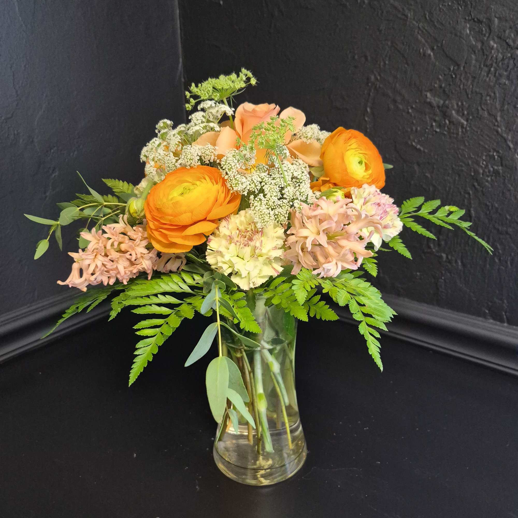 Bright orange ranunculus take center stage in this cheerful flower arrangement, paired