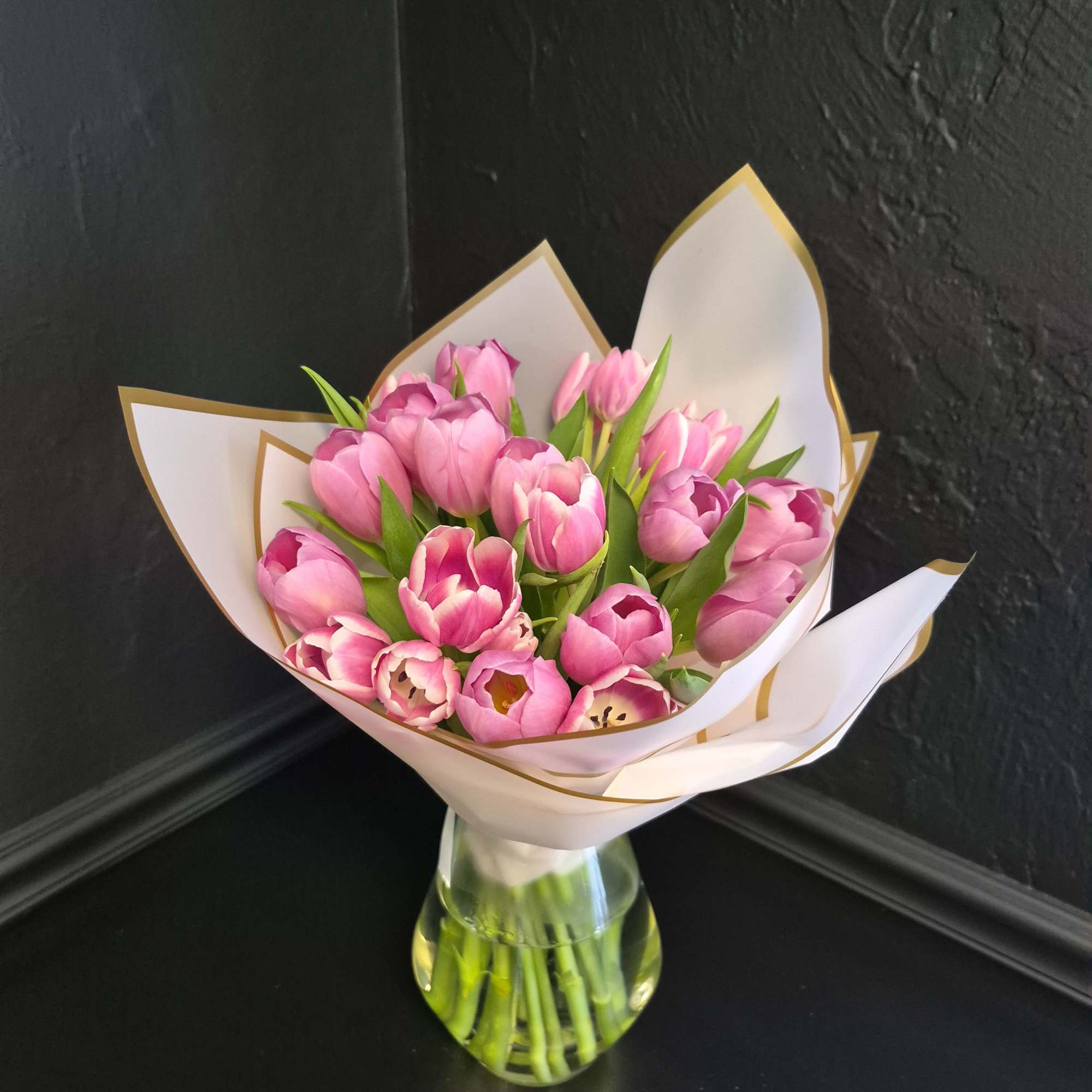 A cluster of bright pink tulips arranged in a compact, hand-tied bouquet