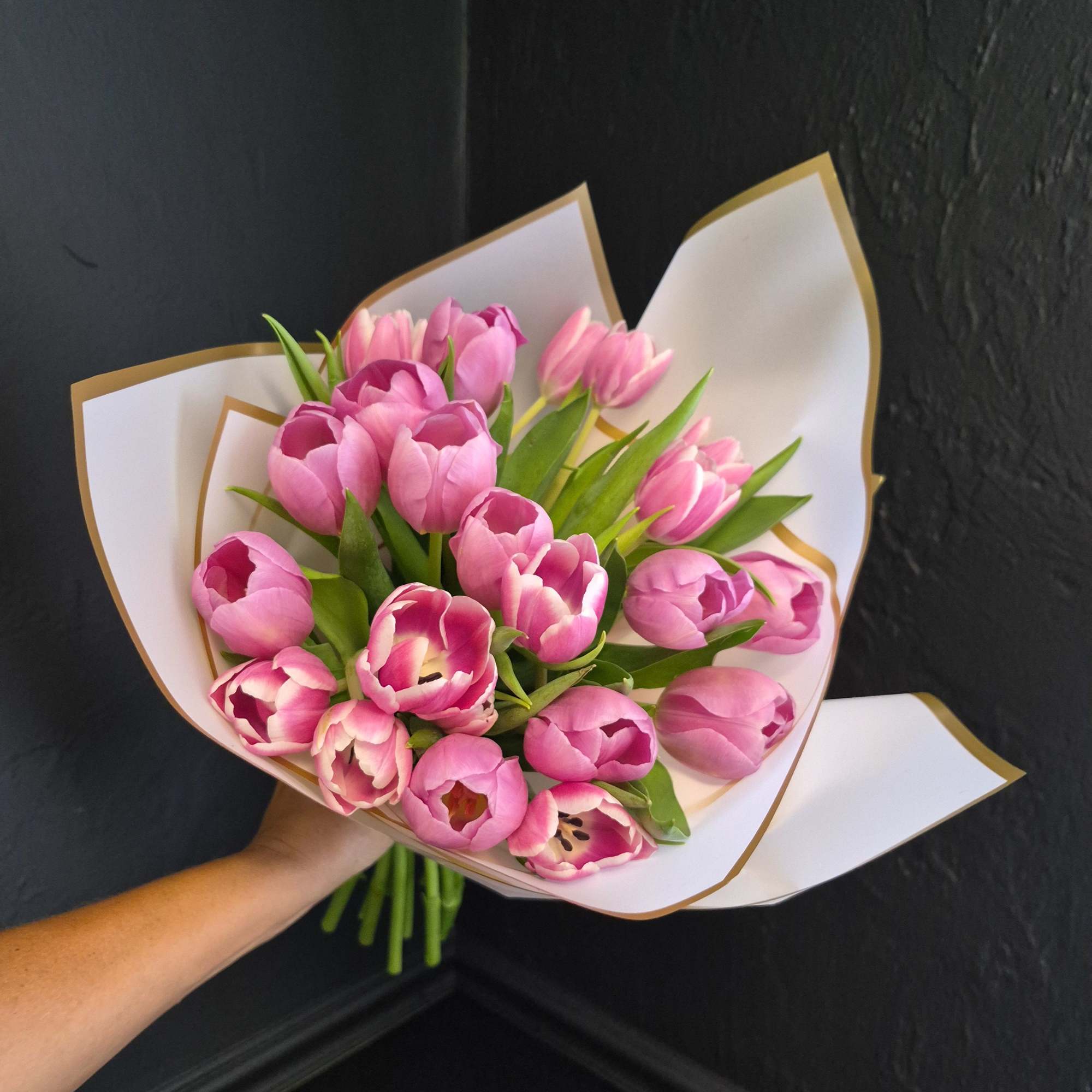 A cluster of bright pink tulips arranged in a compact, hand-tied bouquet