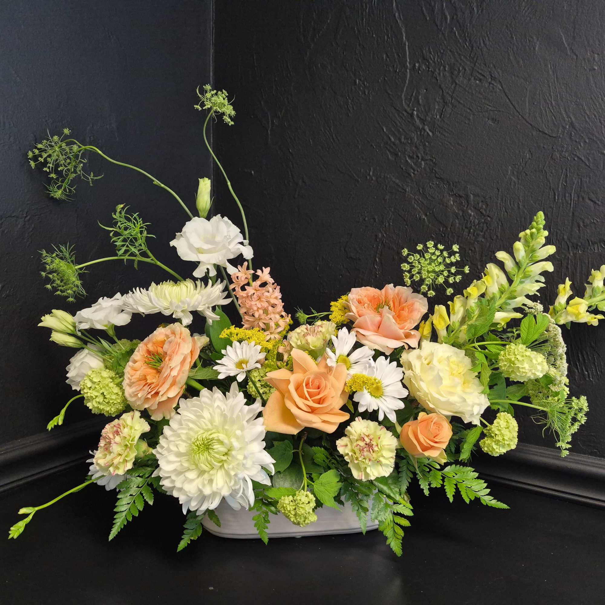 Peach garden roses and airy snapdragons spill from a low white ceramic