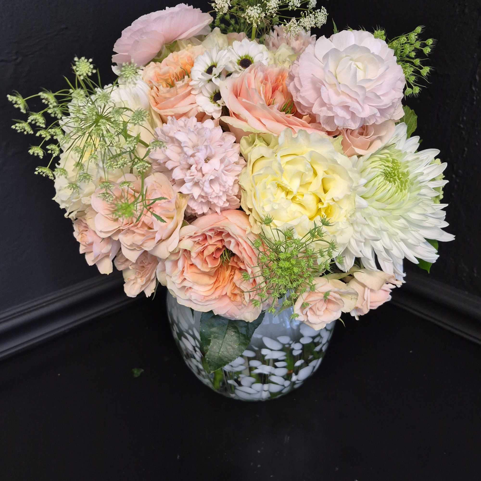 Soft blush roses and creamy peach blooms mingle with pale yellow daisies