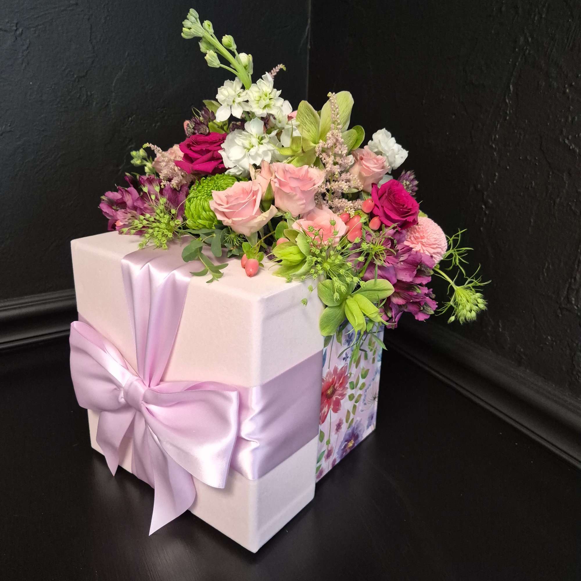 Pink and purple floral arrangement on a gift box with a satin ribbon