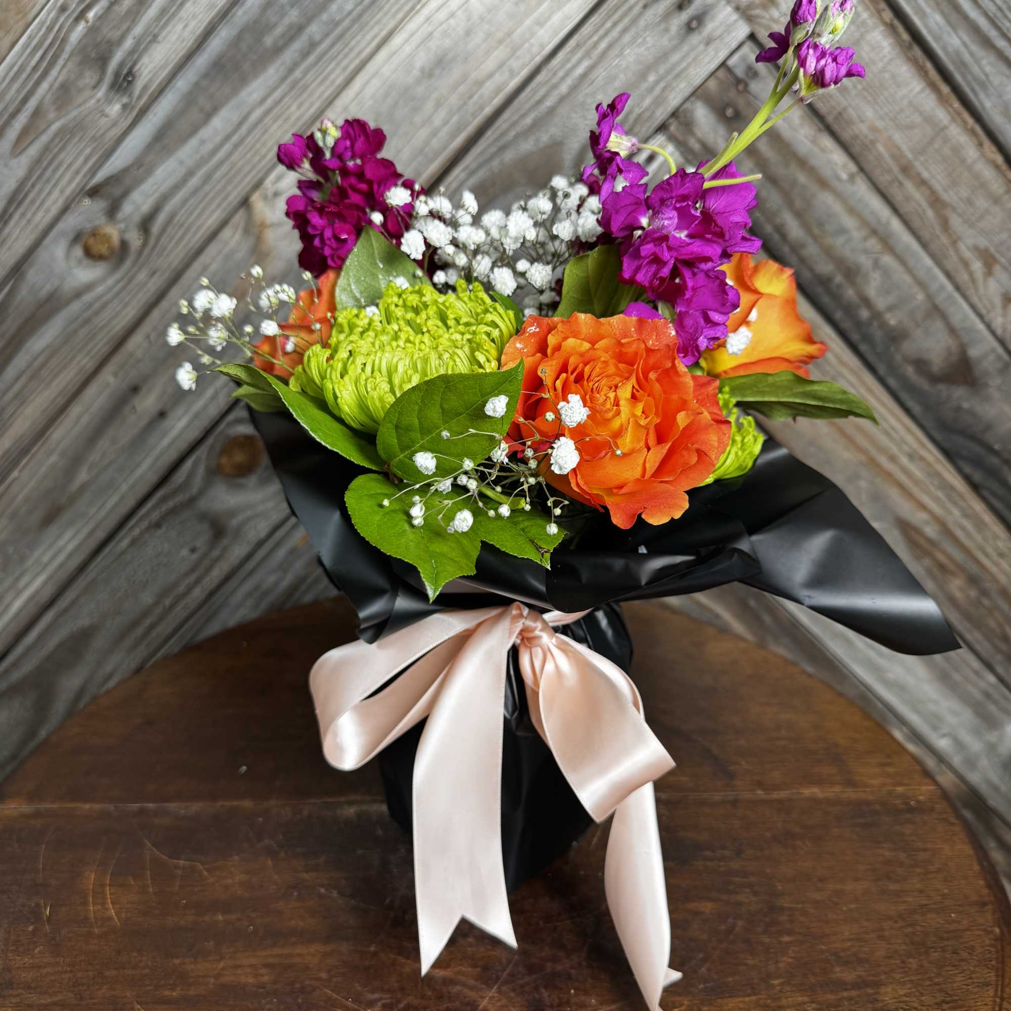 Bouquet of orange and green flowers wrapped in black paper with a pale ribbon