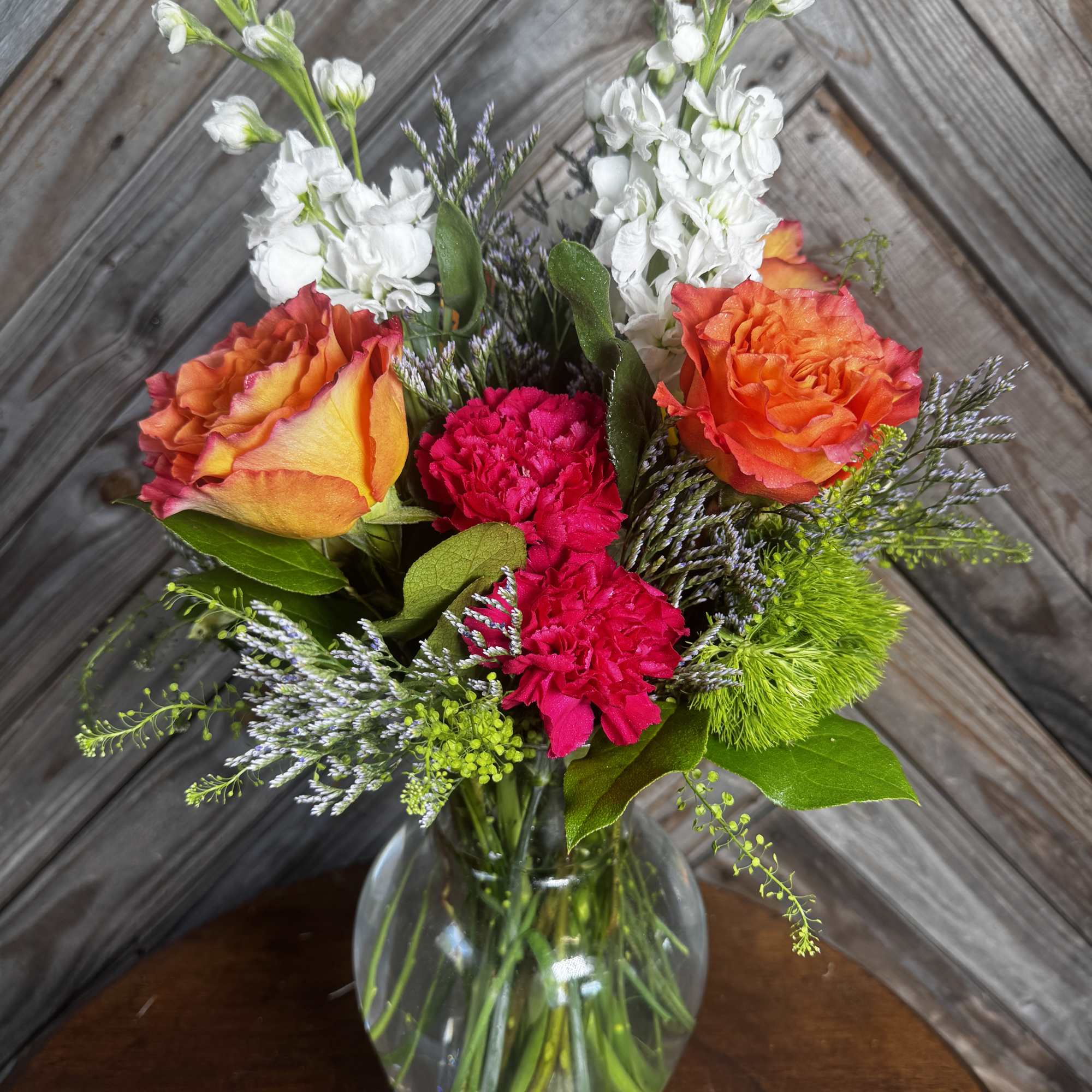 Mixed bouquet of orange roses, white stock, and pink carnations in a glass vase