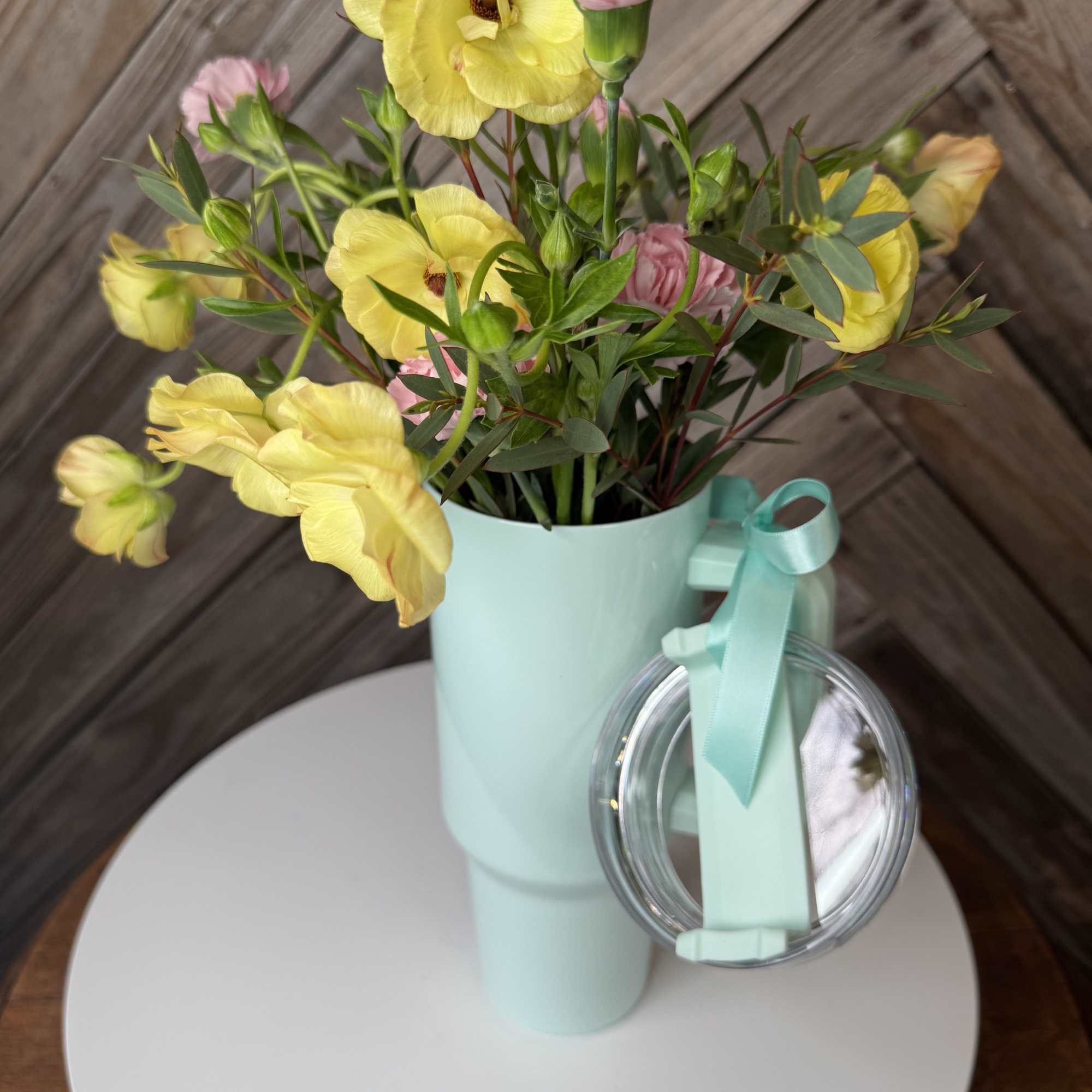 Bouquet of yellow and pink flowers in a mint vase with a ribbon