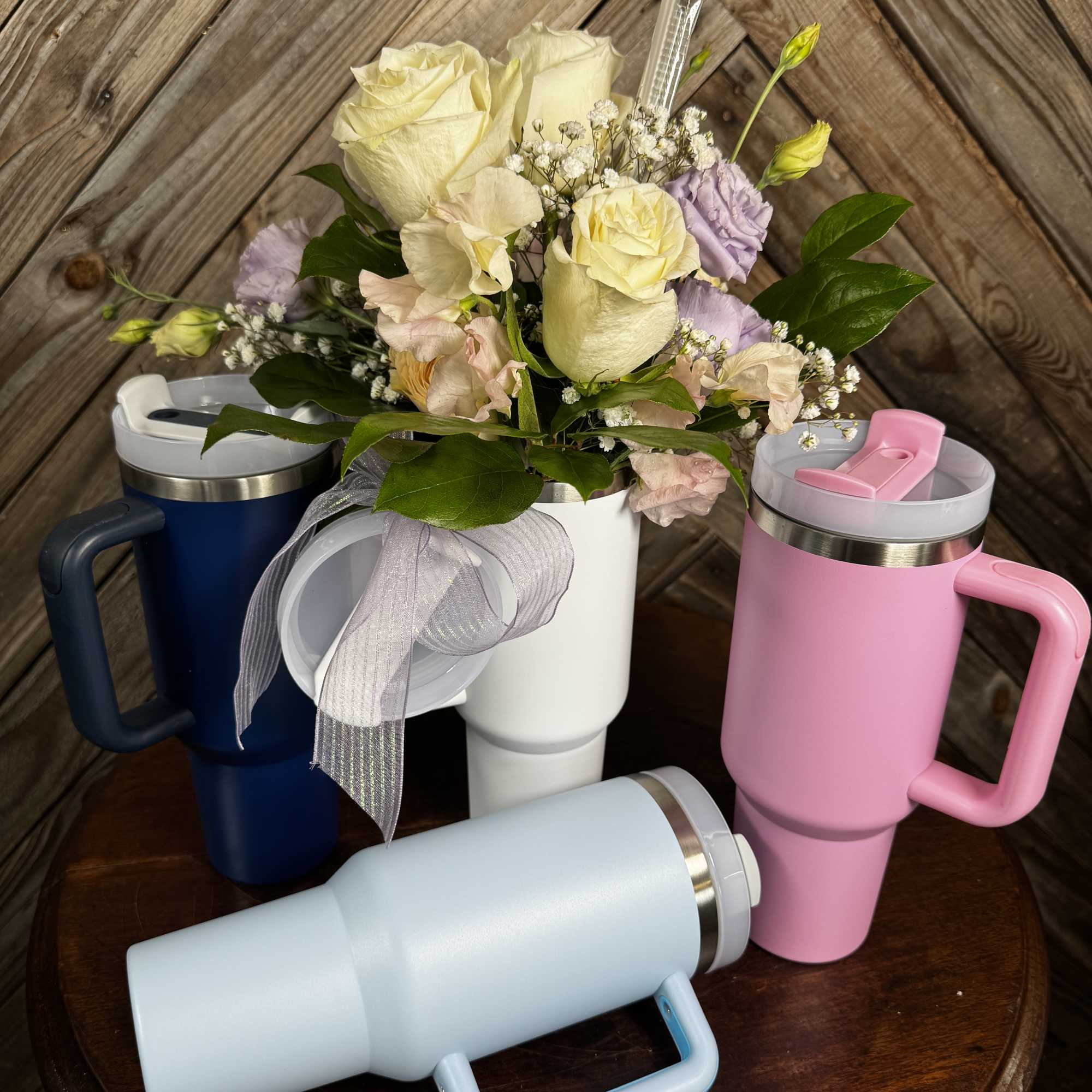 Pastel flower arrangement in a white tumbler with pink, blue, and navy tumblers nearby.