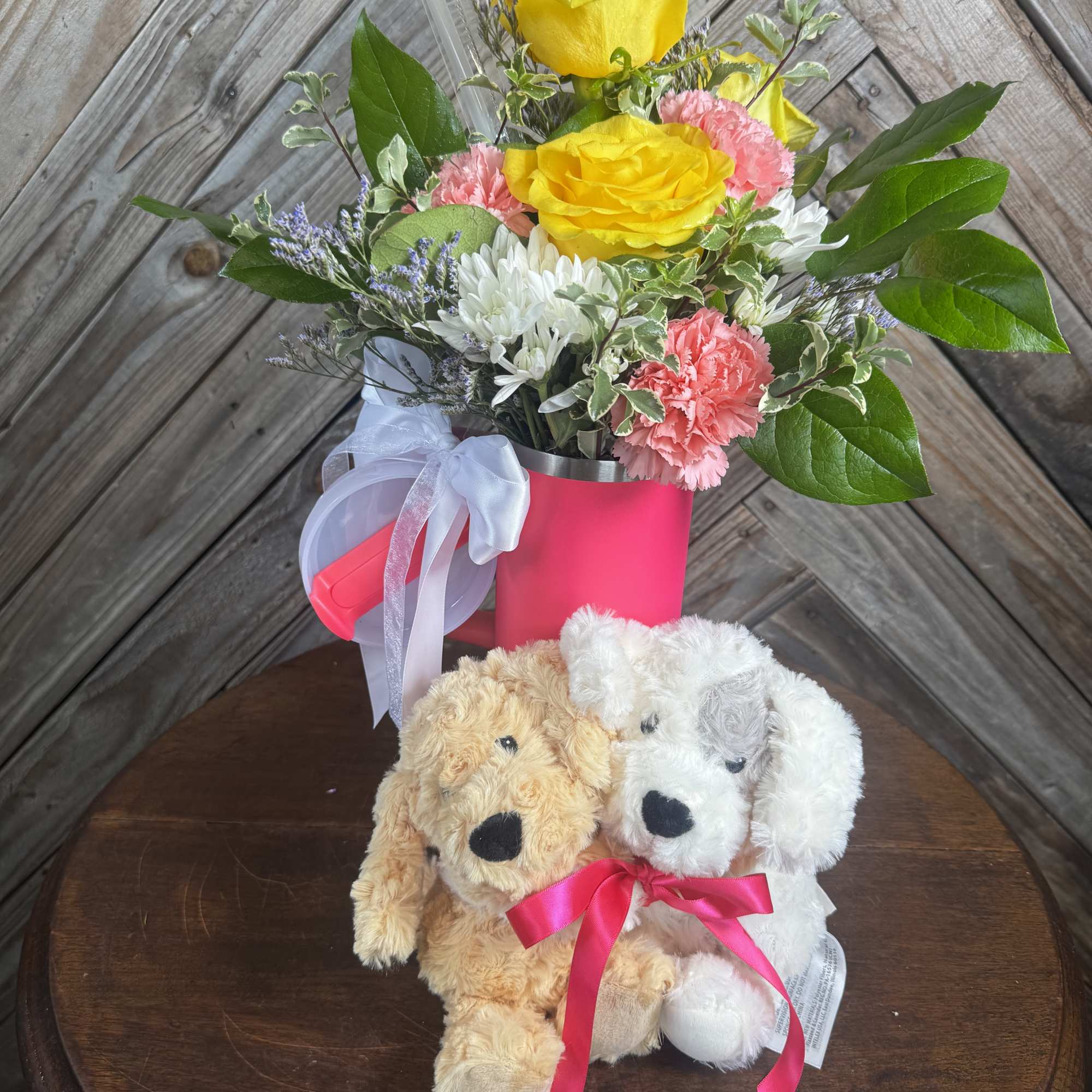 Yellow roses and pink carnations in a pink container with two plush dogs.