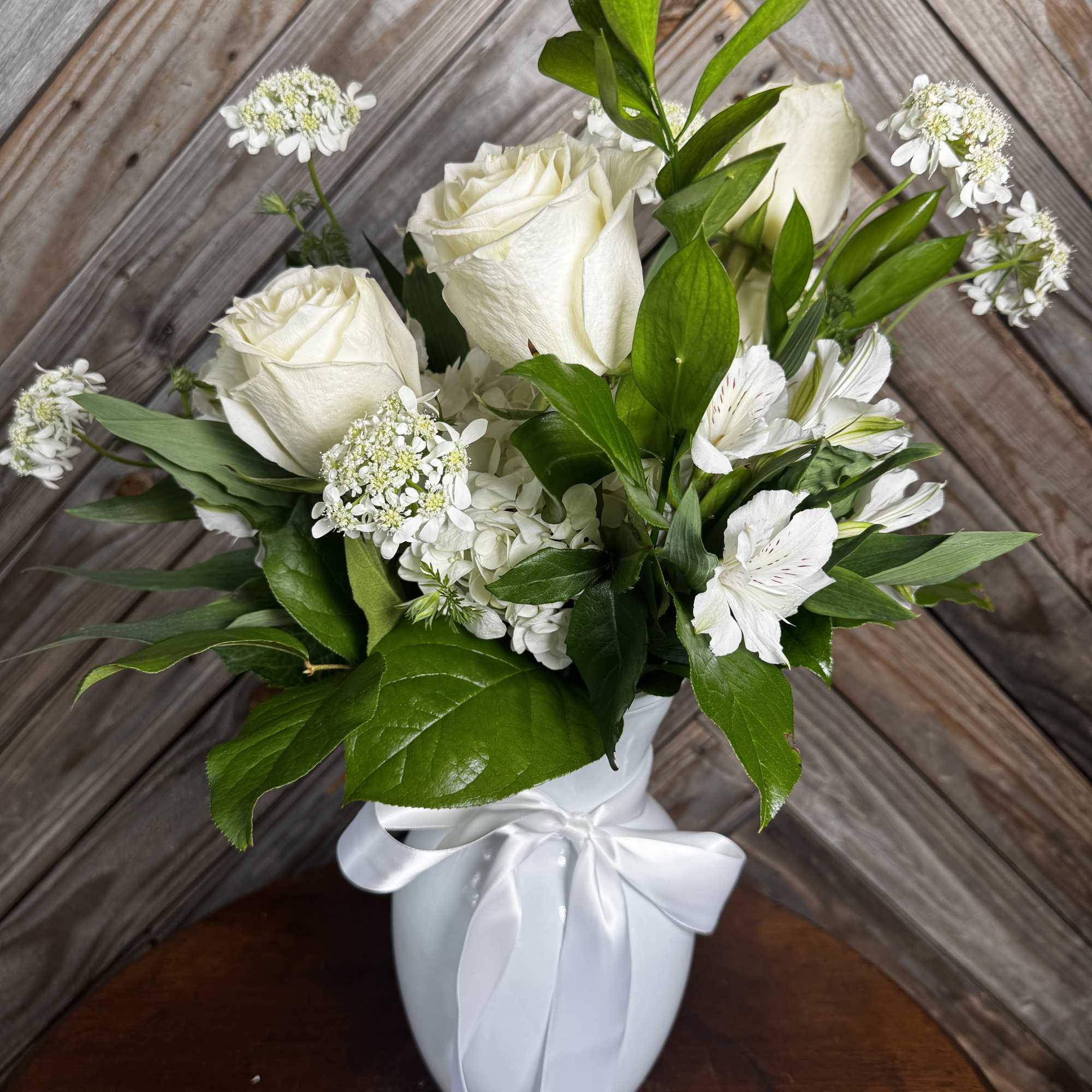White roses and small white flowers in a white vase with a ribbon