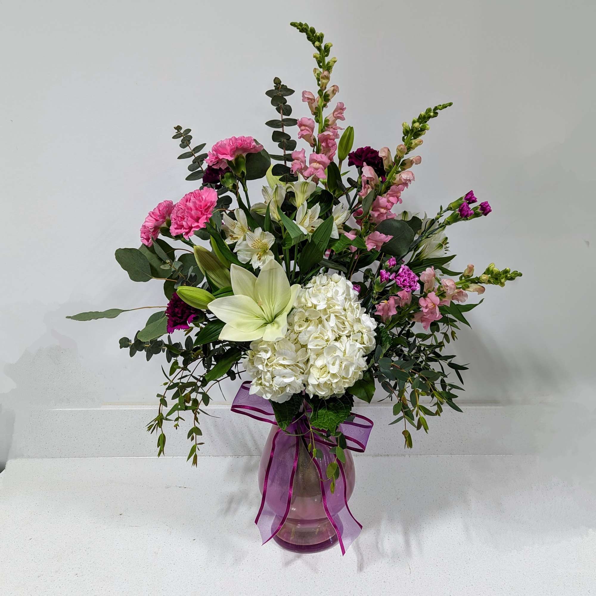 Mixed pink and white flower arrangement in a purple glass vase