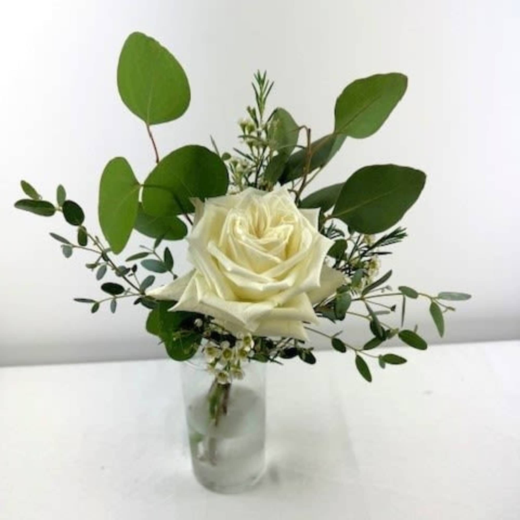 White rose in a small glass vase with greenery
