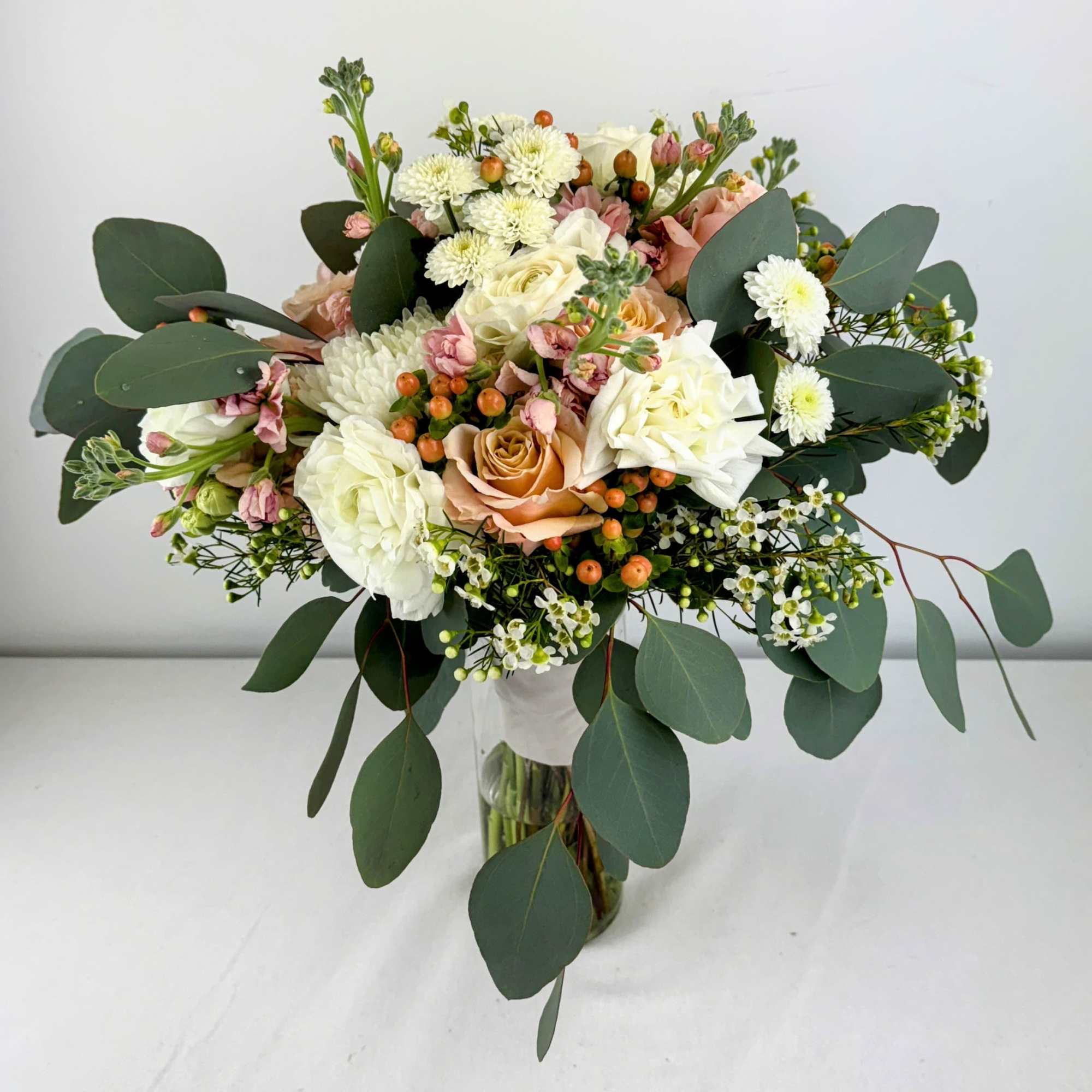 Bouquet of white and peach roses with small white blooms in a glass vase