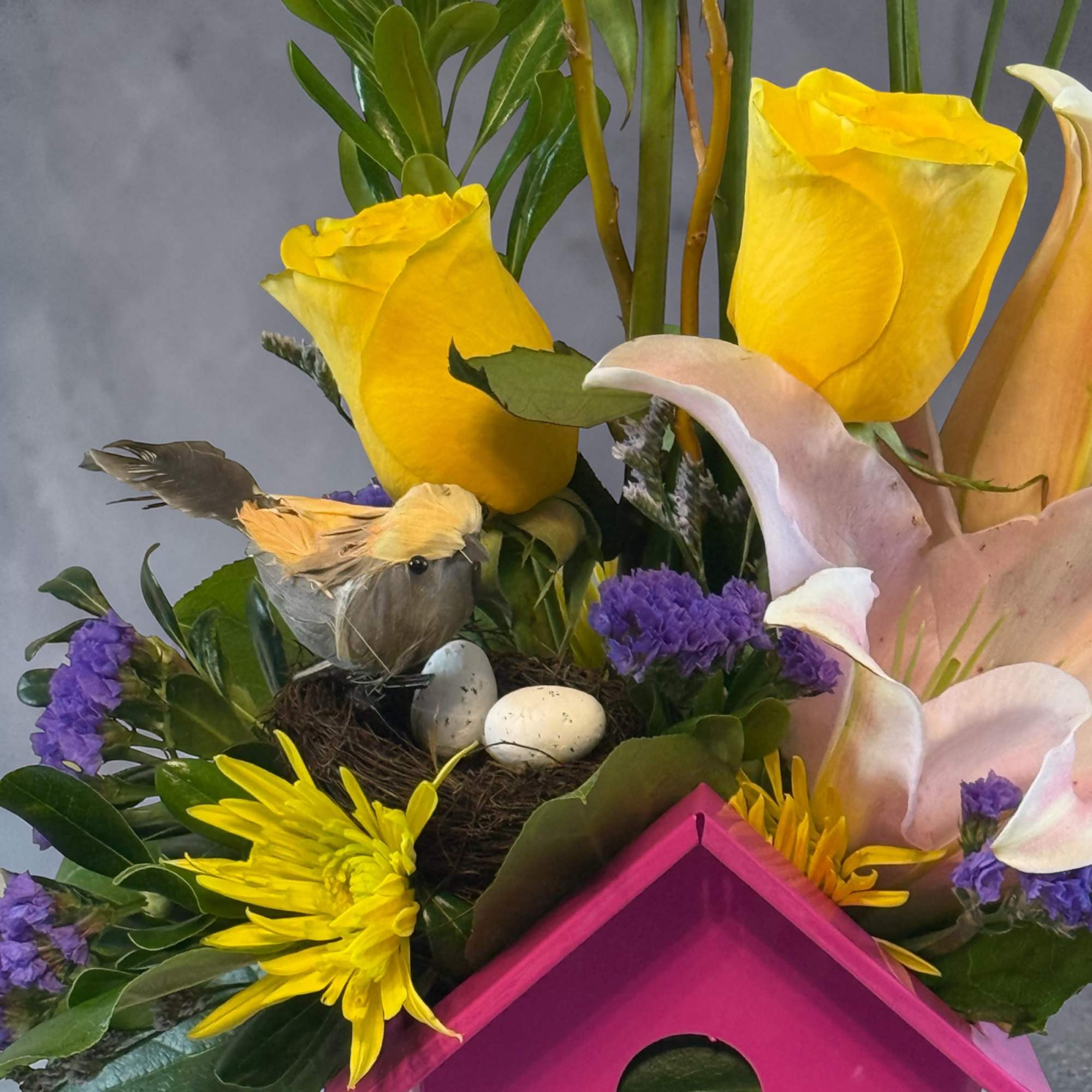 Bouquet with yellow roses, pink calla lilies, and purple flowers around a bird nest