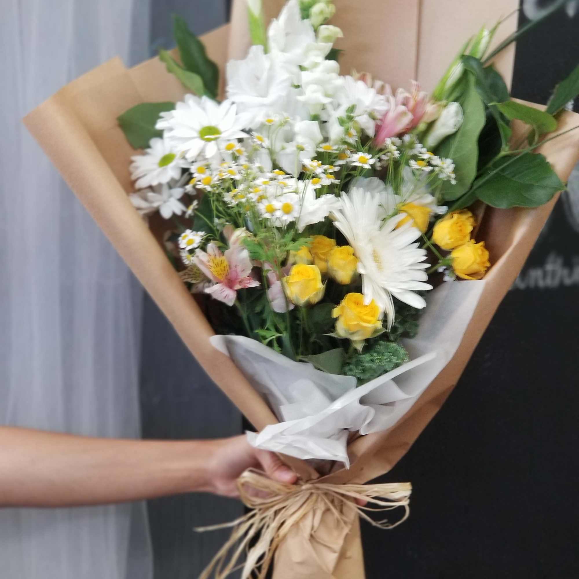 Bouquet of white daisies, yellow roses, and pink alstroemeria in brown paper