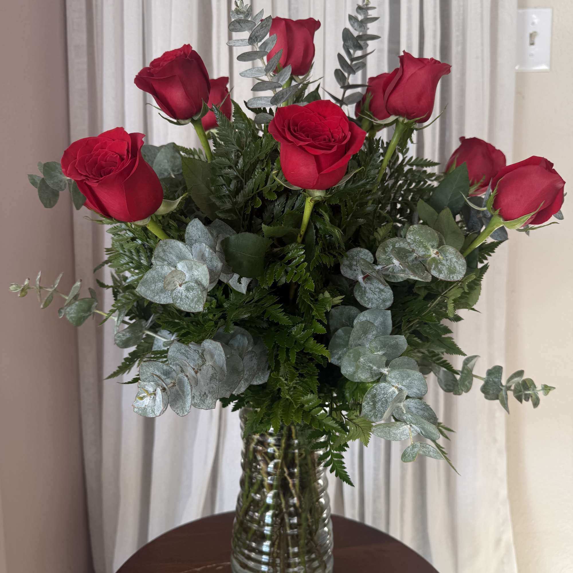 Red roses arranged in a clear glass vase with silvery eucalyptus
