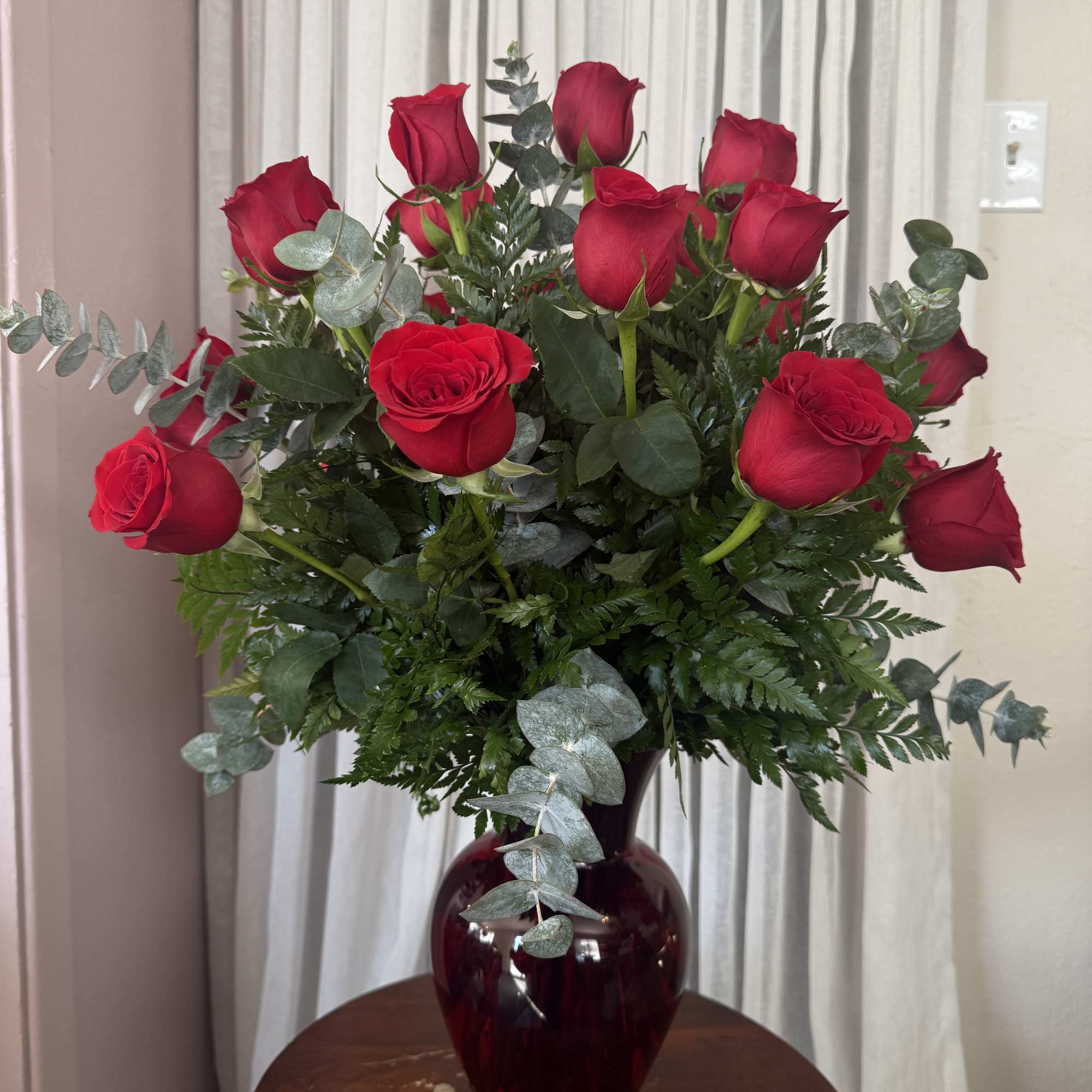 Red roses arranged in a burgundy glass vase