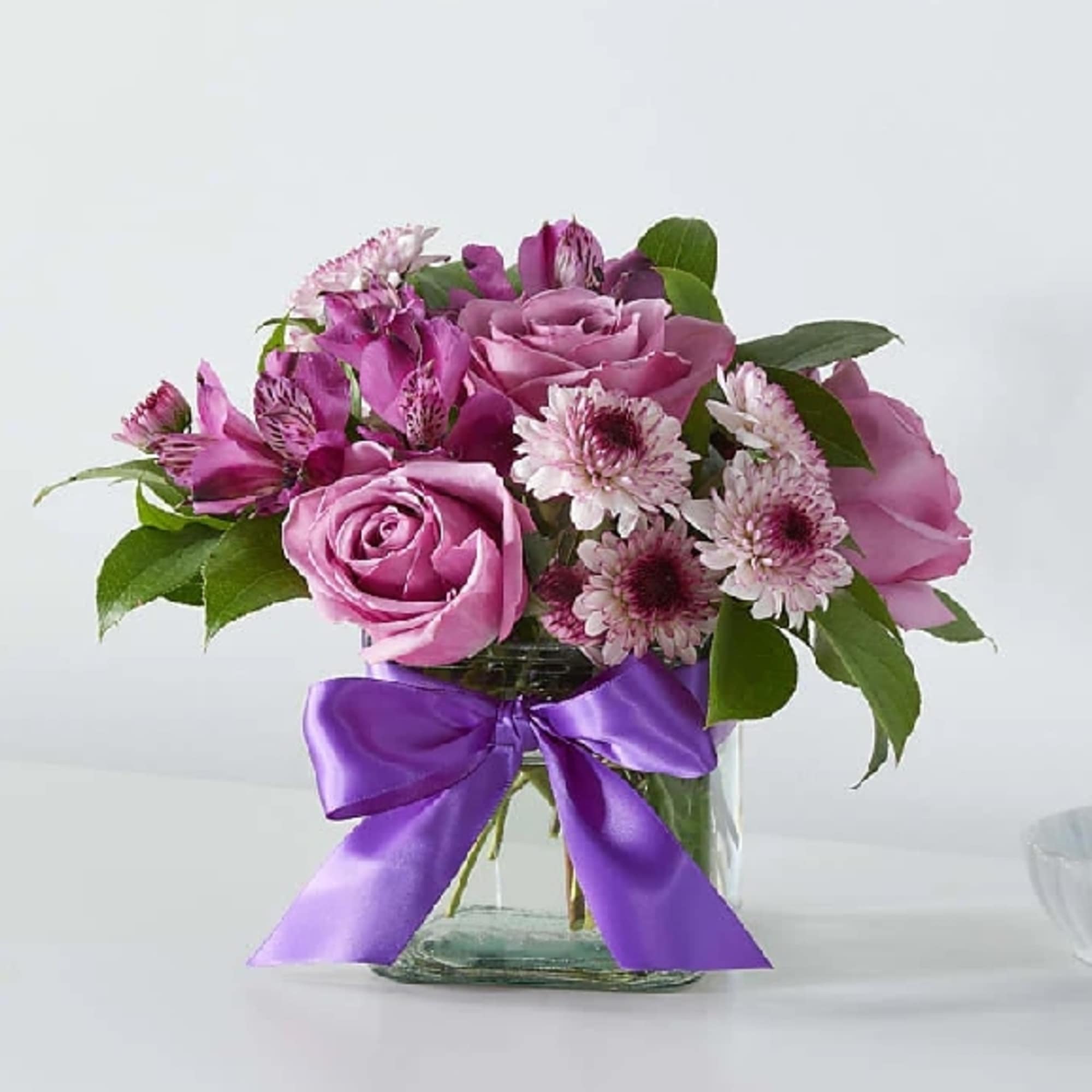 Pink roses and daisy-like flowers in a glass vase with a purple ribbon