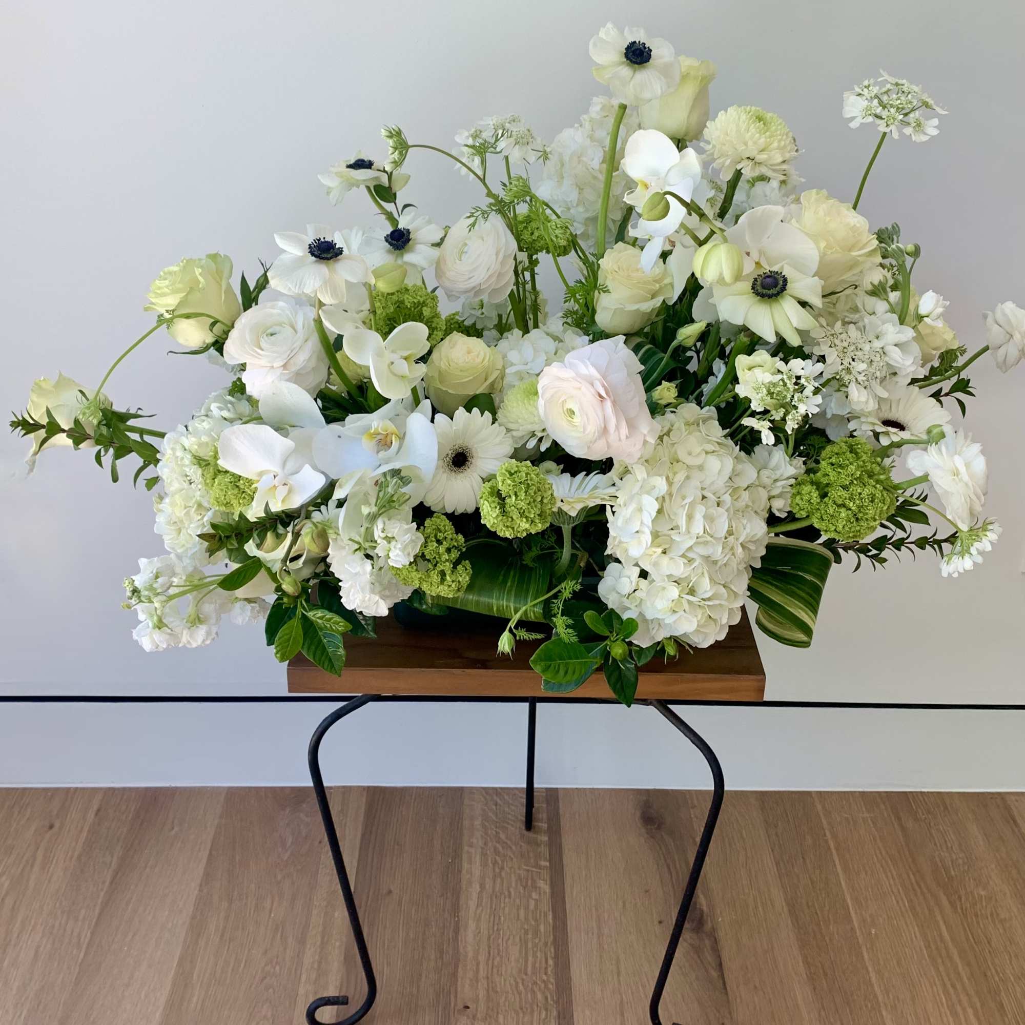 White floral arrangement with orchids, ranunculus, and hydrangeas in a wooden container