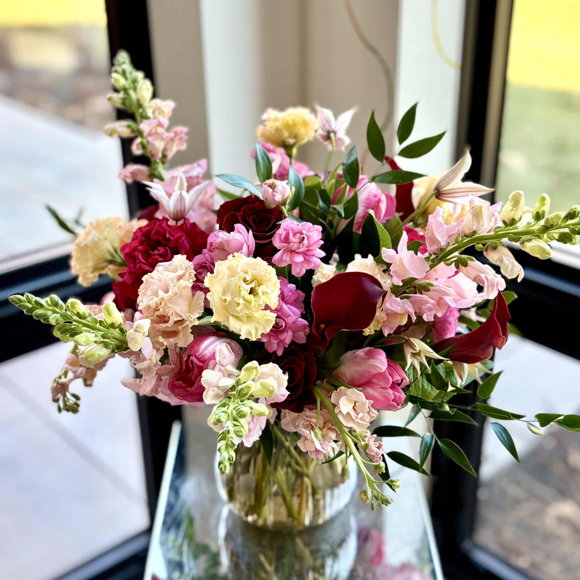 Mixed bouquet of pink, red, and cream flowers in a glass vase