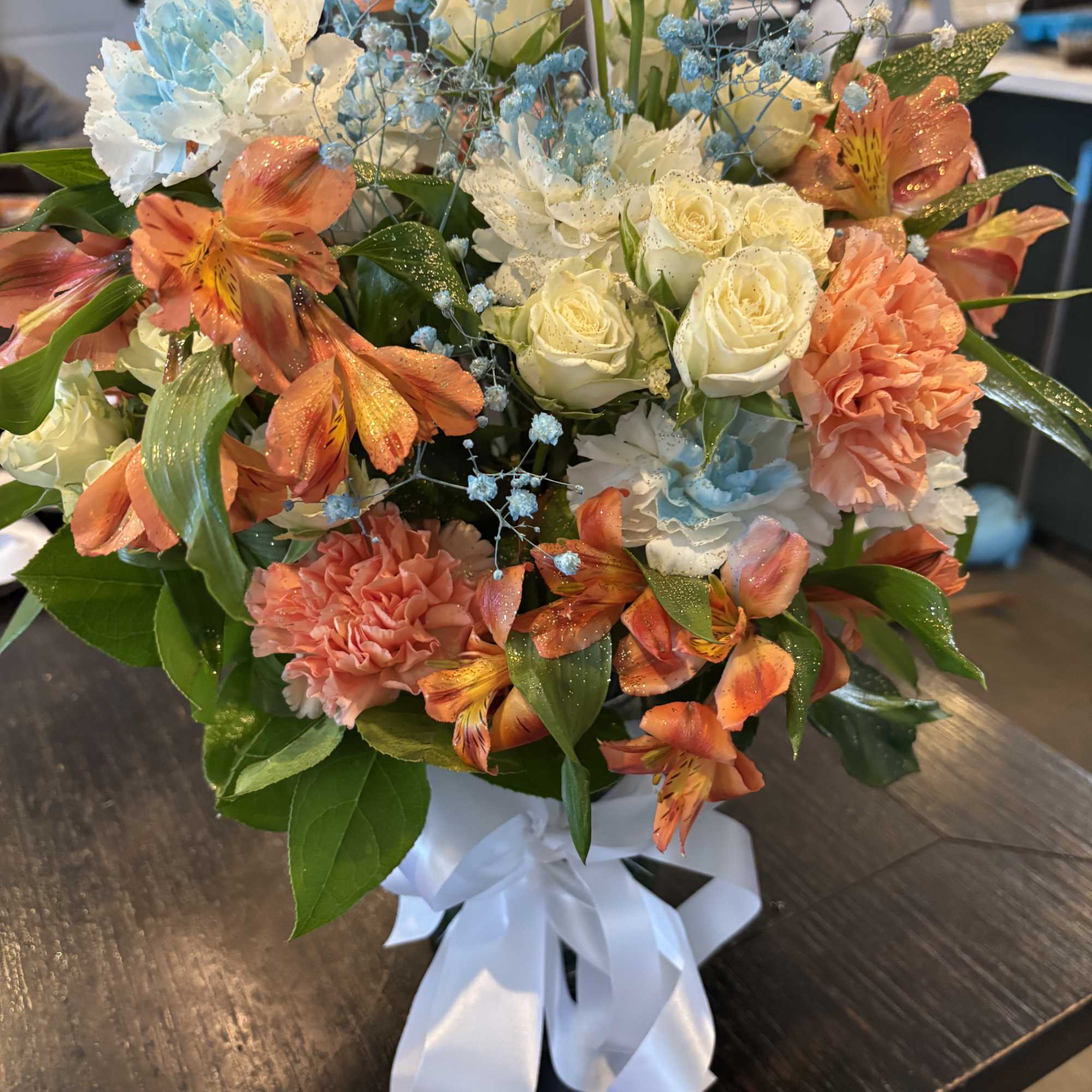 Bouquet of cream roses, peach carnations, and orange alstroemeria in a white vase