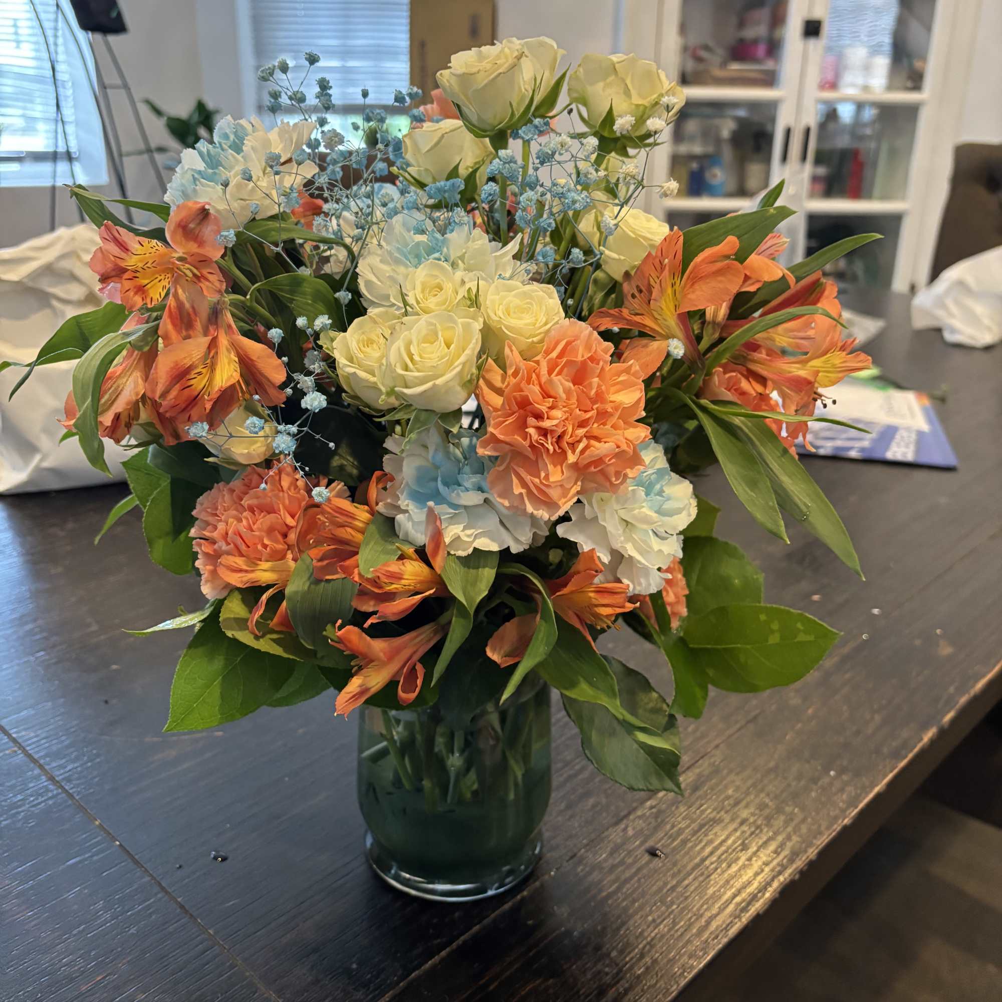 Bouquet of cream roses, orange alstroemeria, and blue filler in a glass vase