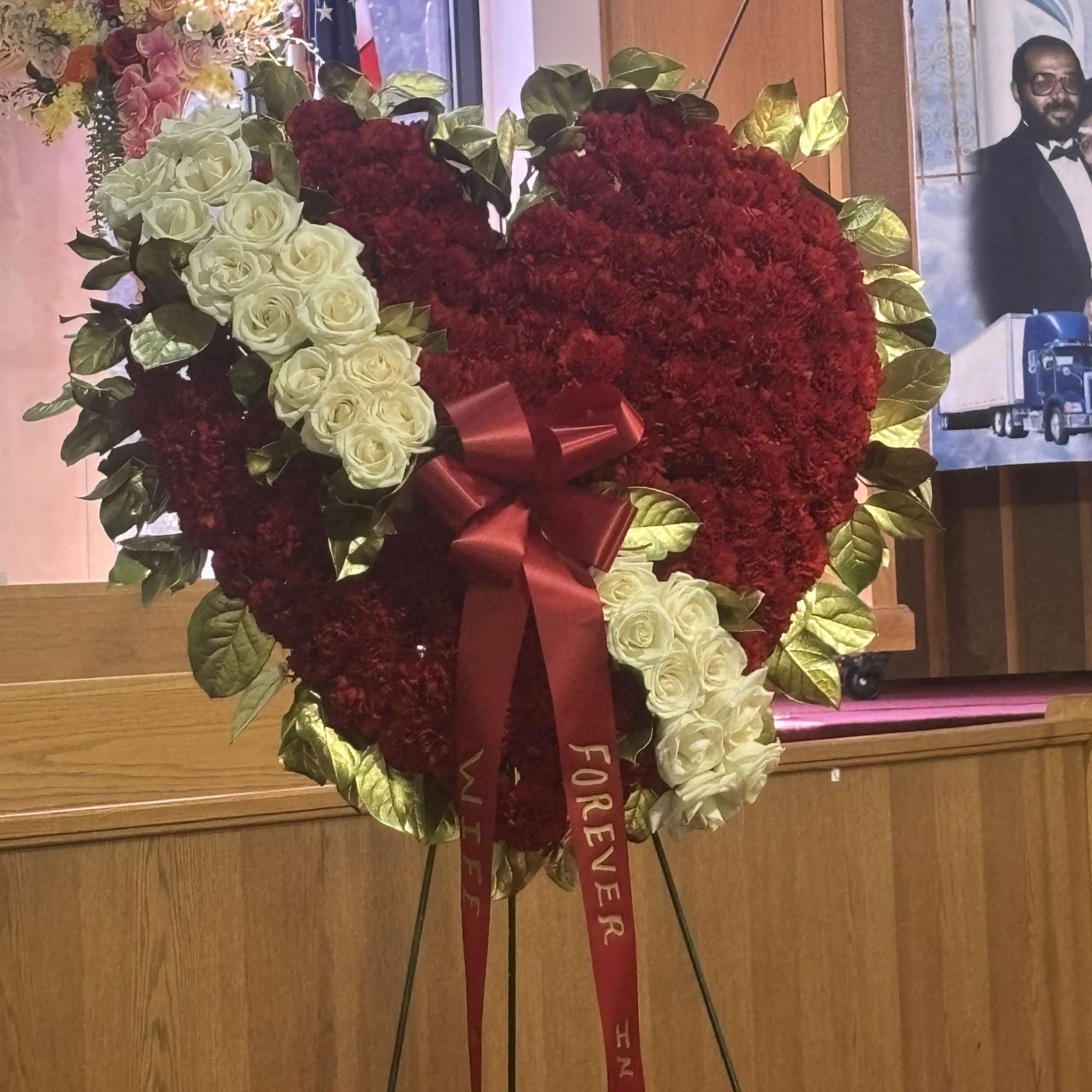Heart-shaped red floral wreath with white roses and a red ribbon on an easel