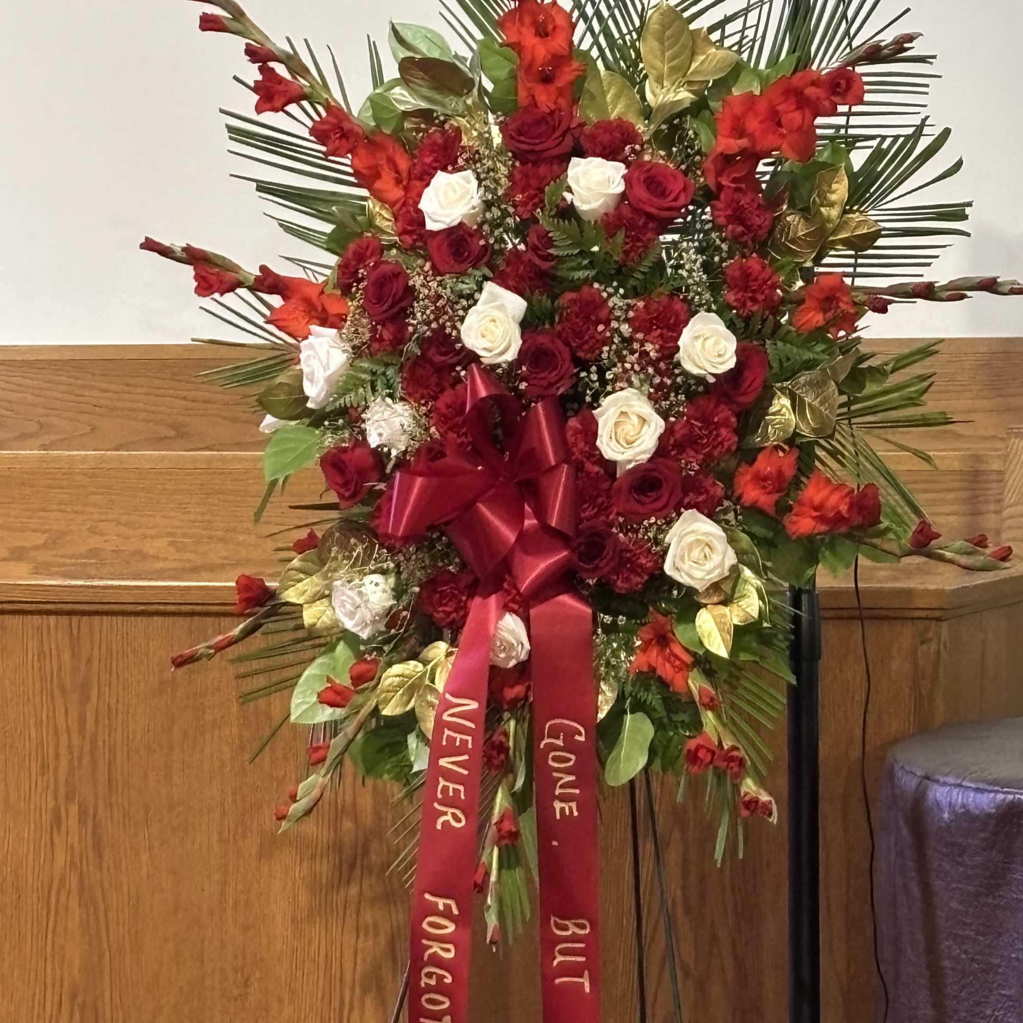 Large red and white floral standing spray with ribbon on an easel