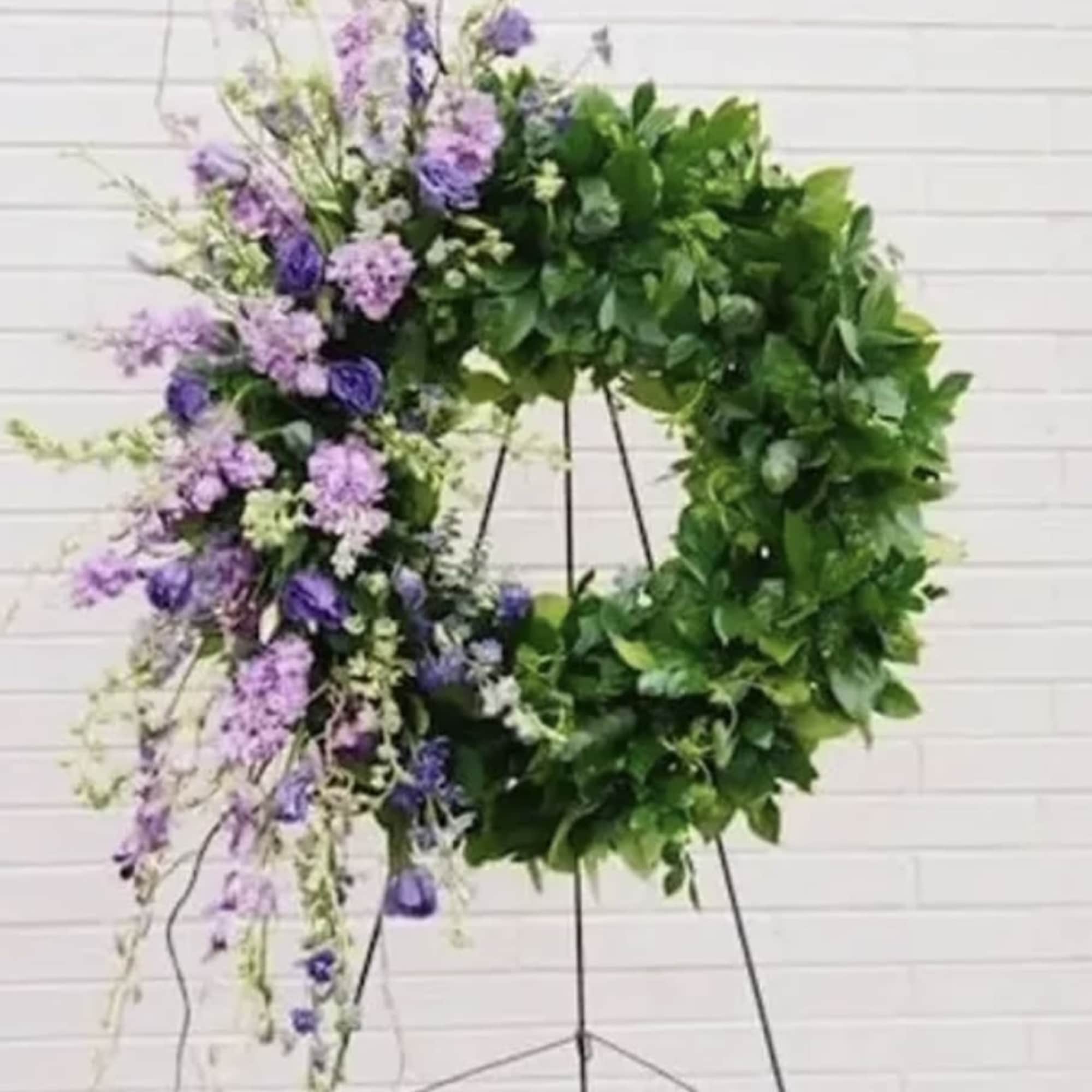 Large floral wreath with purple flowers and dense green foliage on a stand