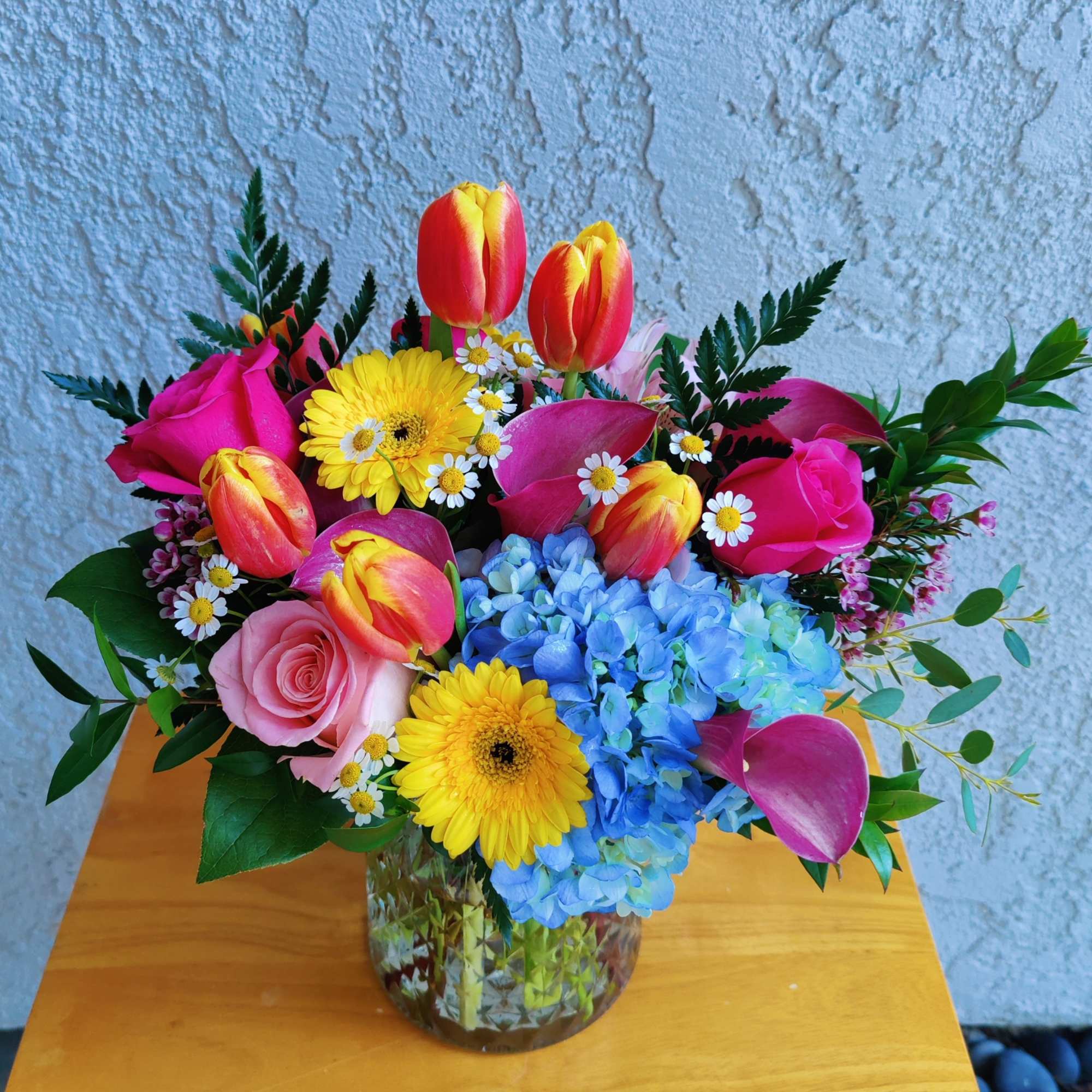 Colorful bouquet of tulips, roses, gerbera daisies, hydrangeas, and small daisies in a glass vase
