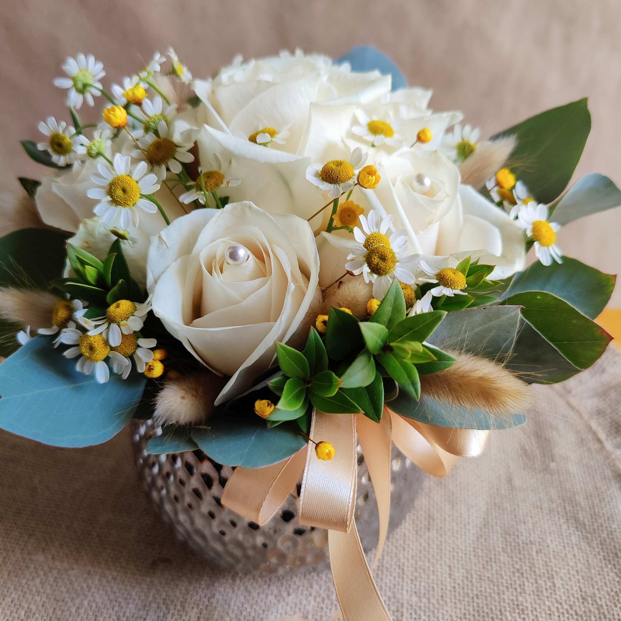 White rose bouquet with small daisy-like flowers and a ribbon-tied vase