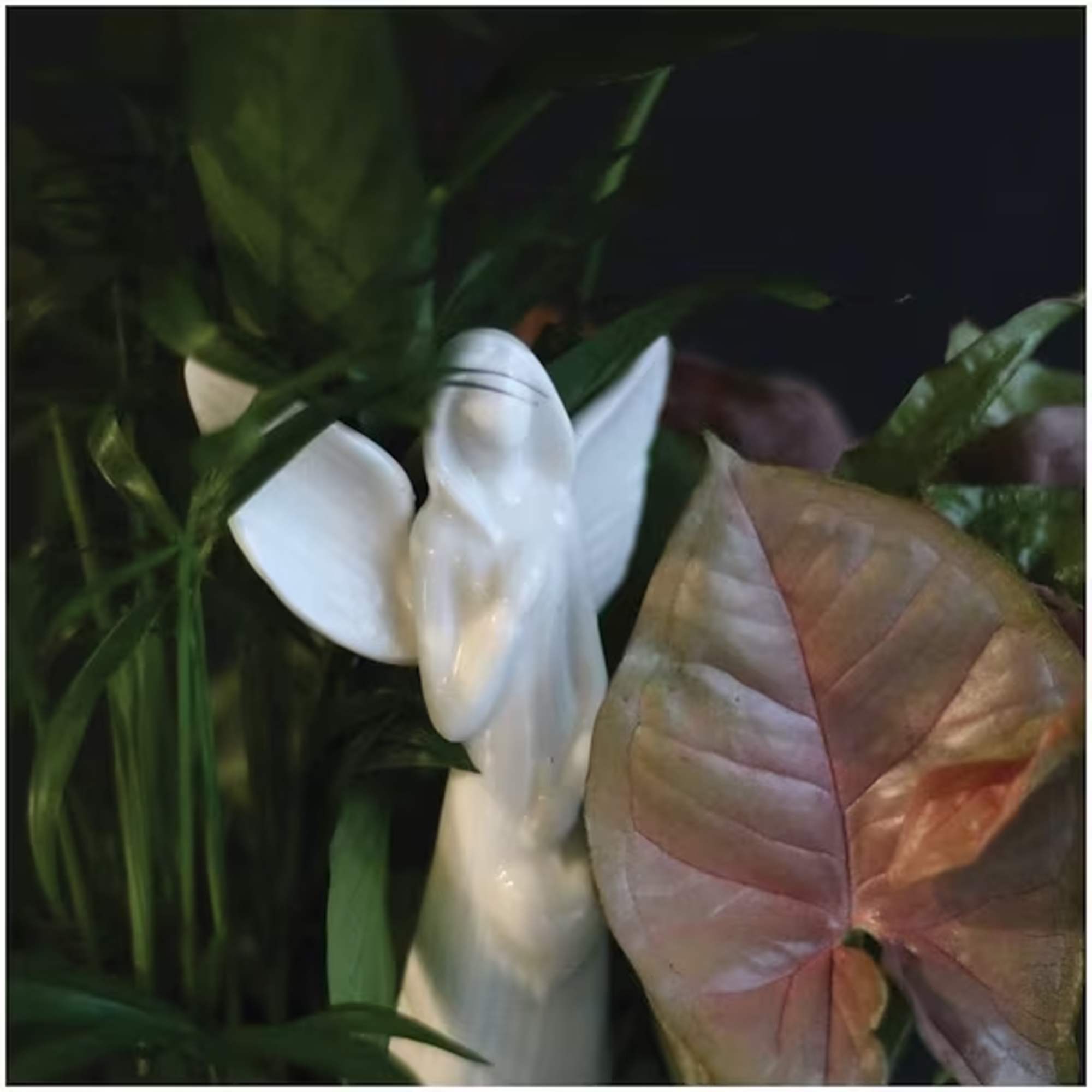 White angel figurine among green plants and a pinkish leaf